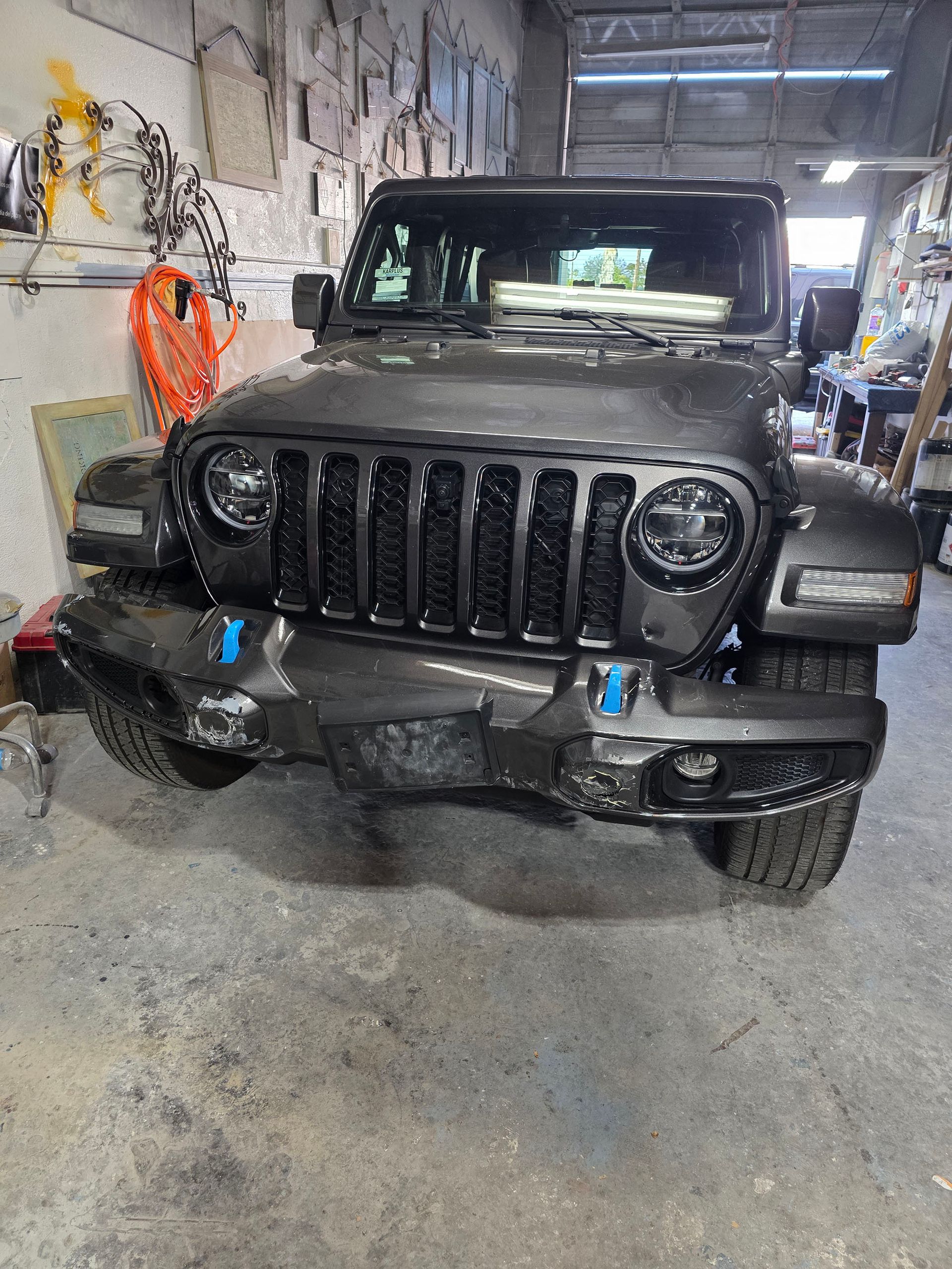 Black Jeep Wrangler inside a garage, front view with blue tow hooks and a winch bumper.