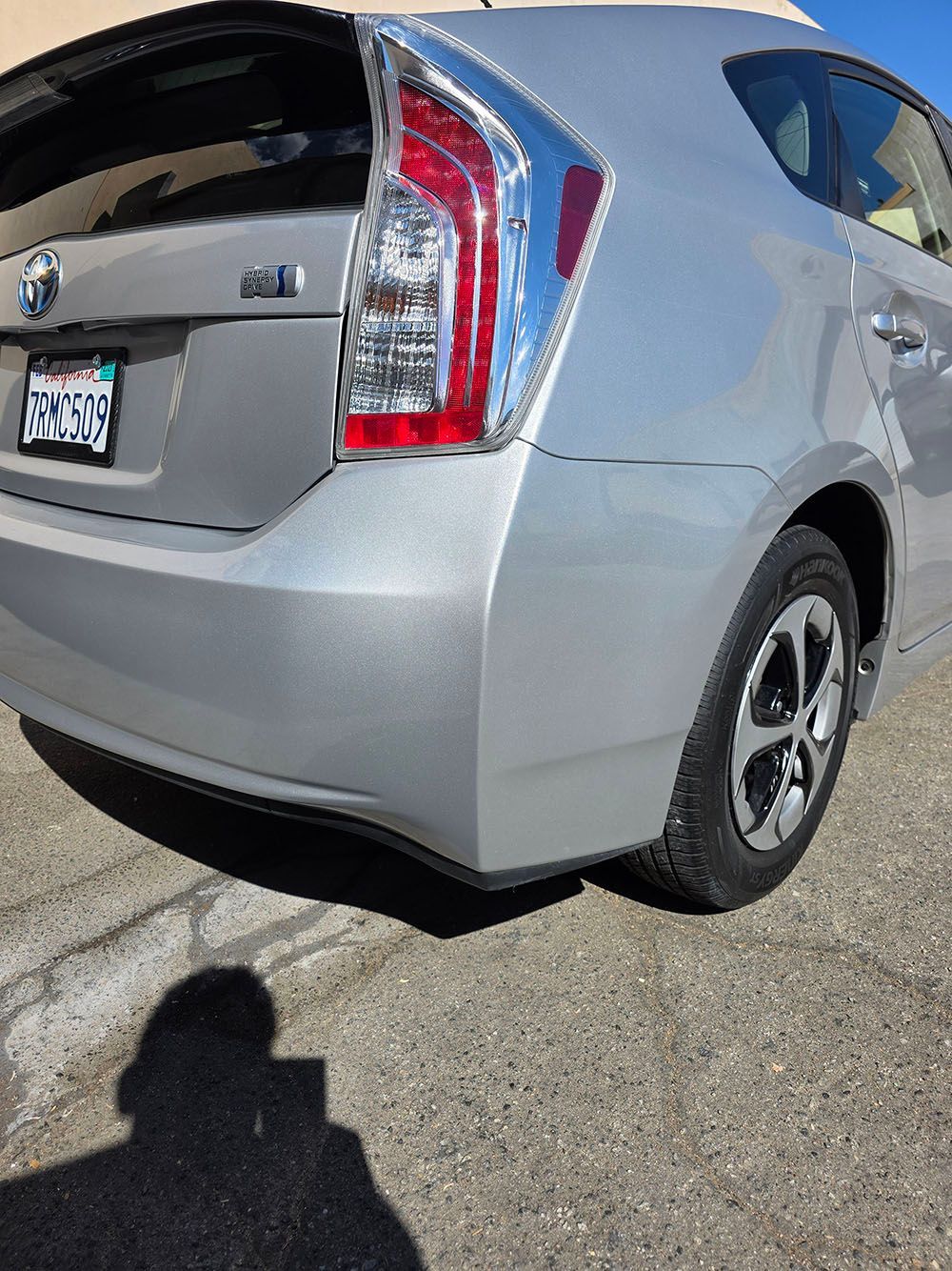 Silver Toyota Prius parked in a sunny lot, rear and side view visible.