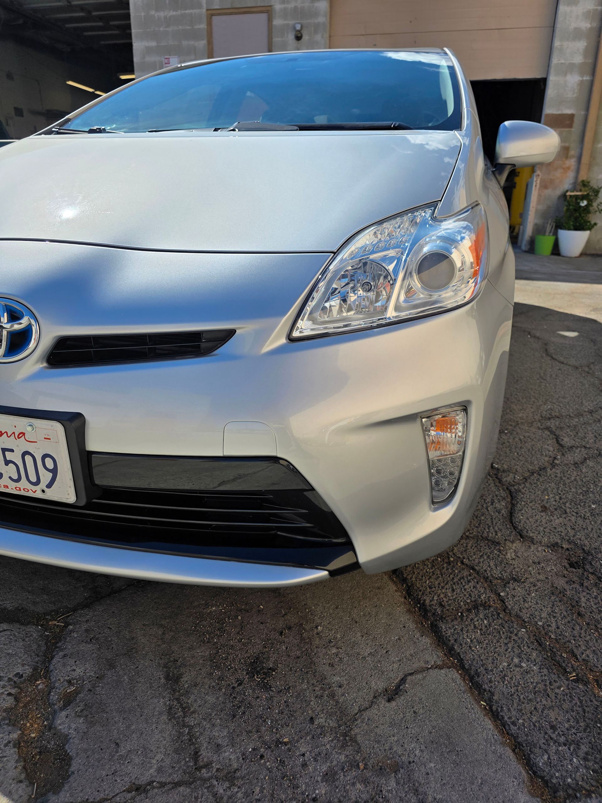 Silver Toyota Prius parked in a driveway, front view on cracked pavement.