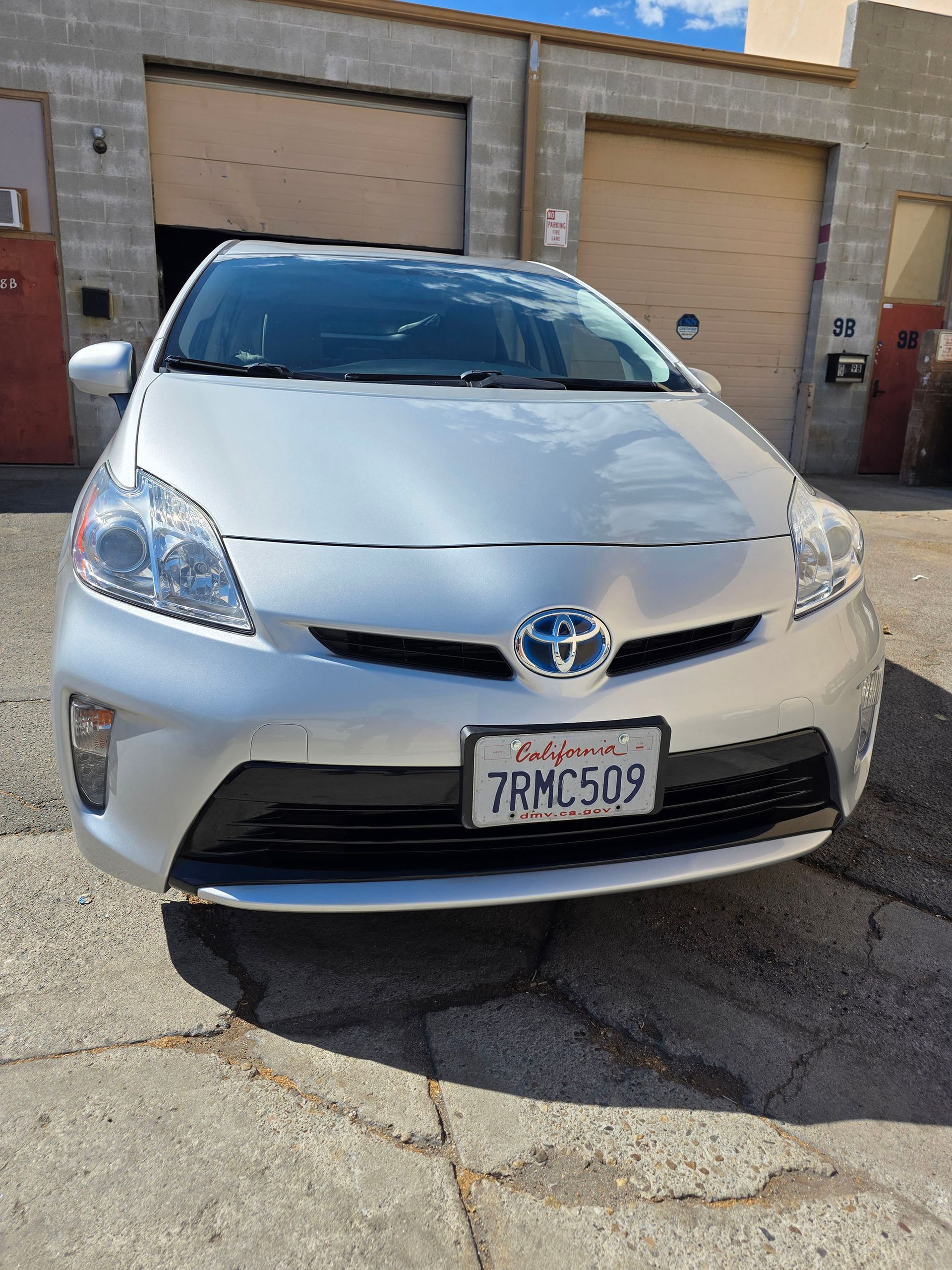 Silver Toyota Prius parked in front of garage doors on a cracked street, front view
