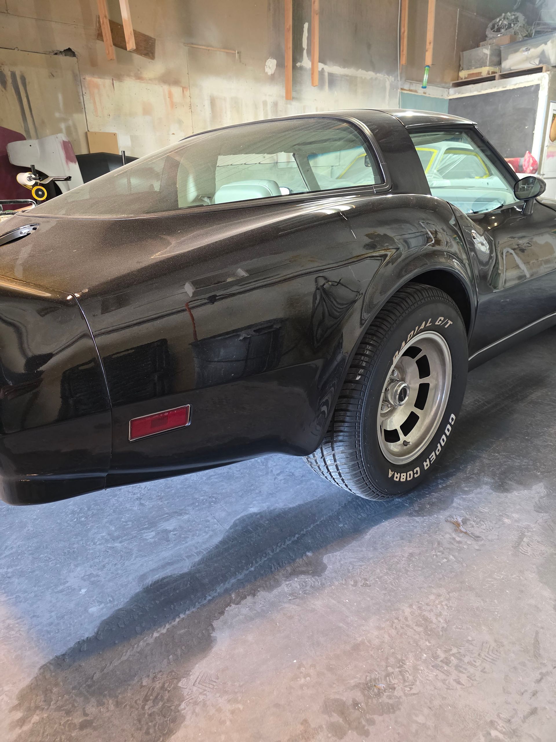 Black classic sports car parked indoors in a garage, rear three-quarter view.