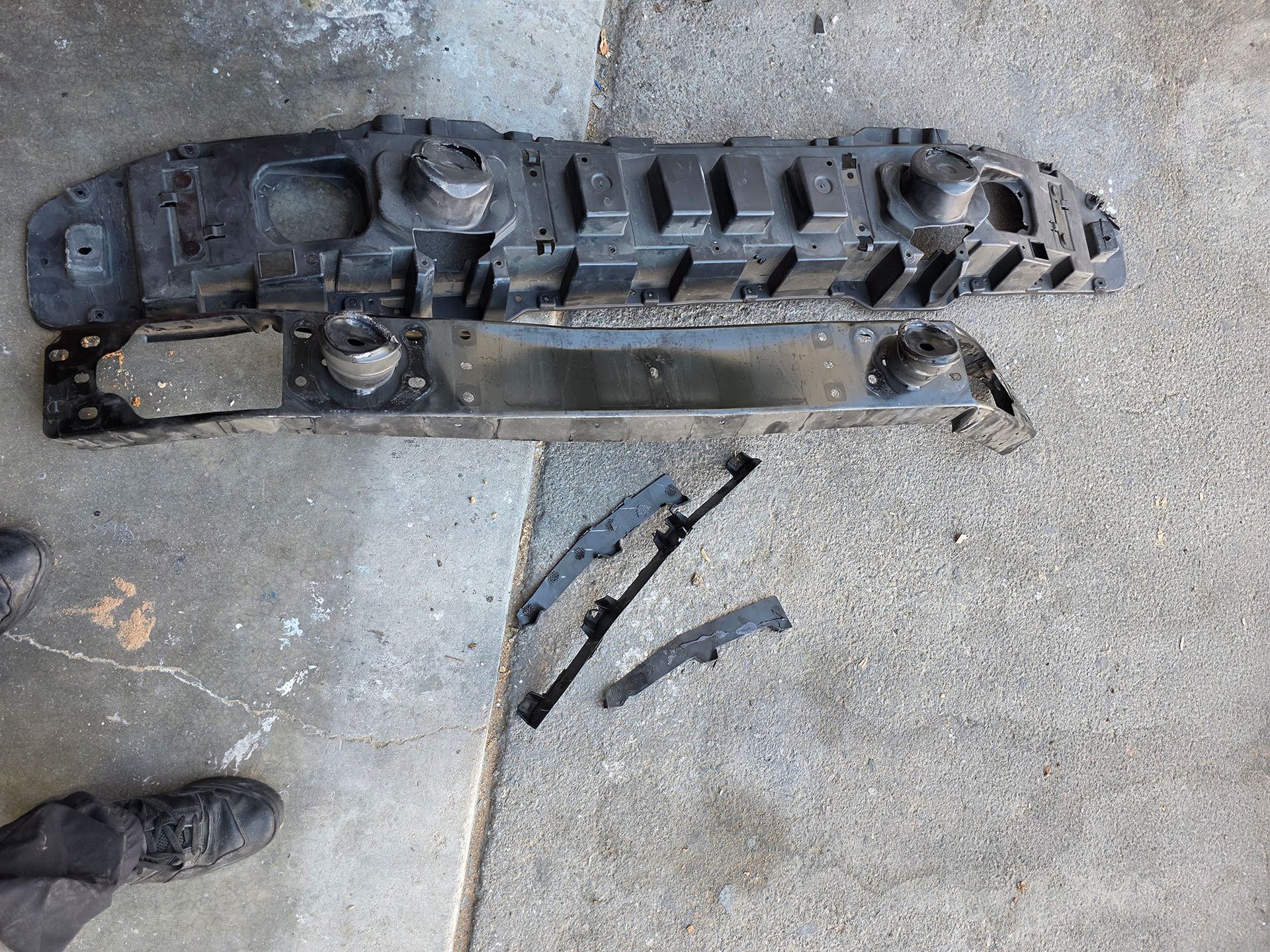 Broken black plastic car grille and trim pieces scattered on concrete floor