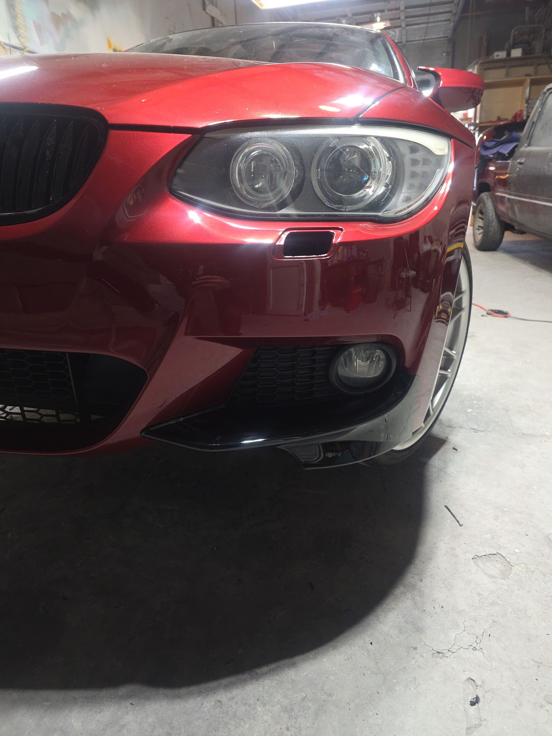 Front of a red car in a garage, showing the headlights and grille.