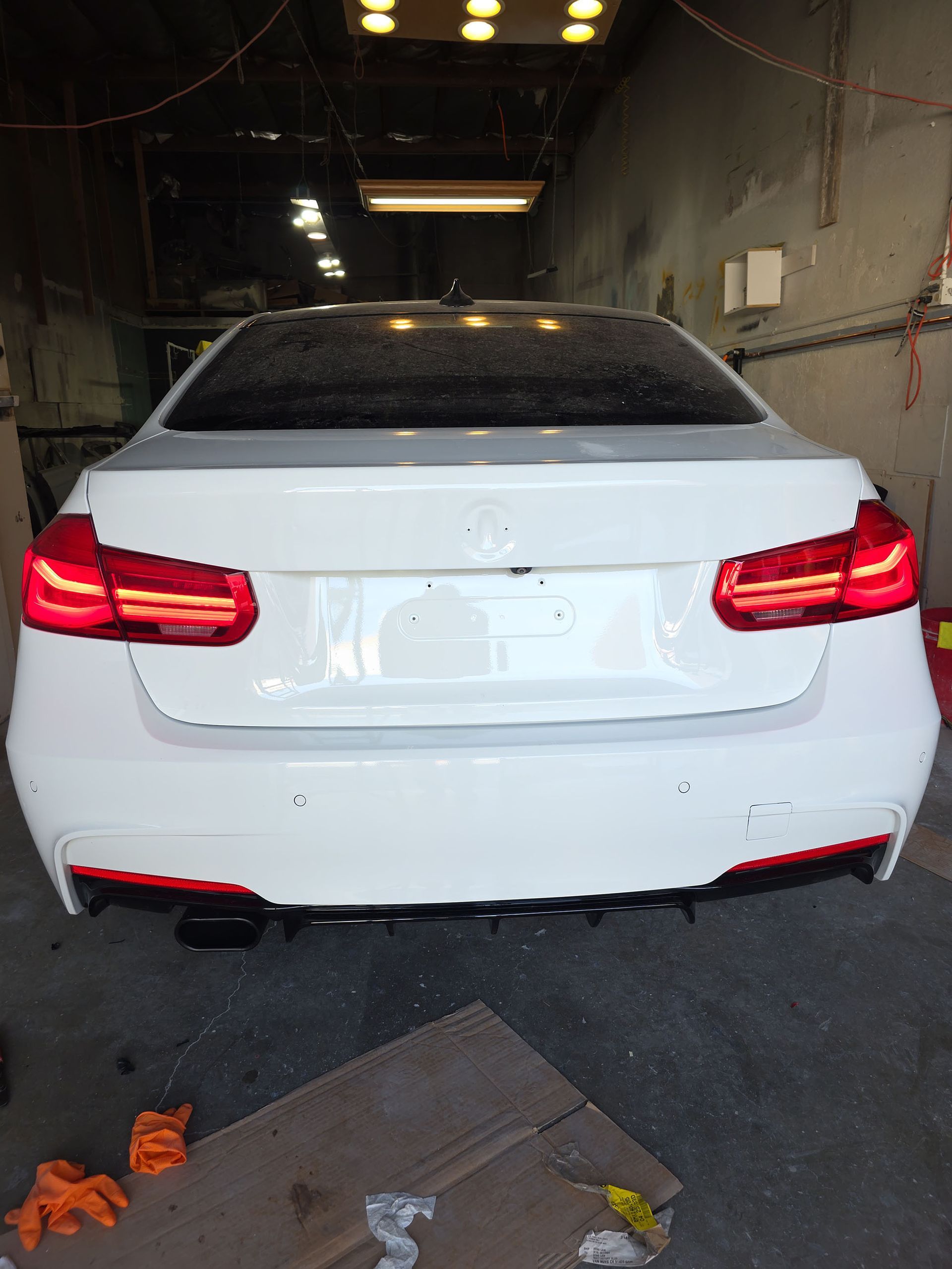 White sedan viewed from the rear in an indoor car wash or garage, taillights glowing red.