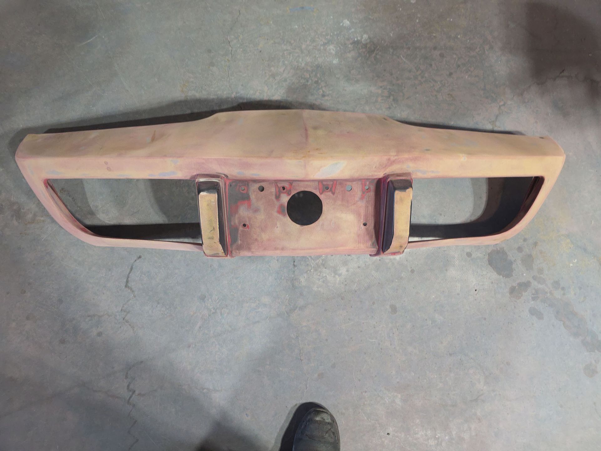 Dusty pink car front bumper with black grille openings, shown on a gray floor