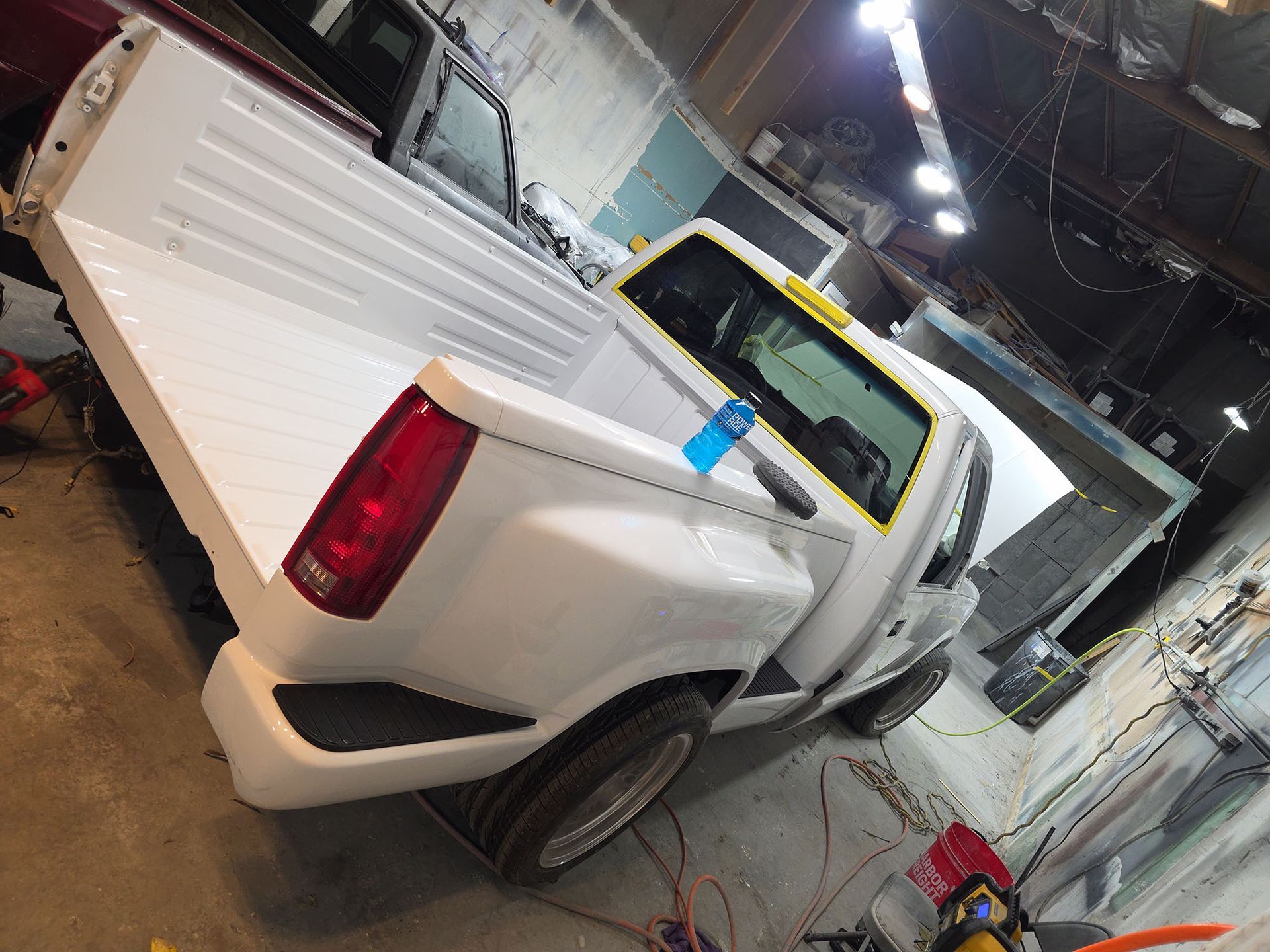 White pickup truck in a garage with a blue-taped rear window and raised bed sides