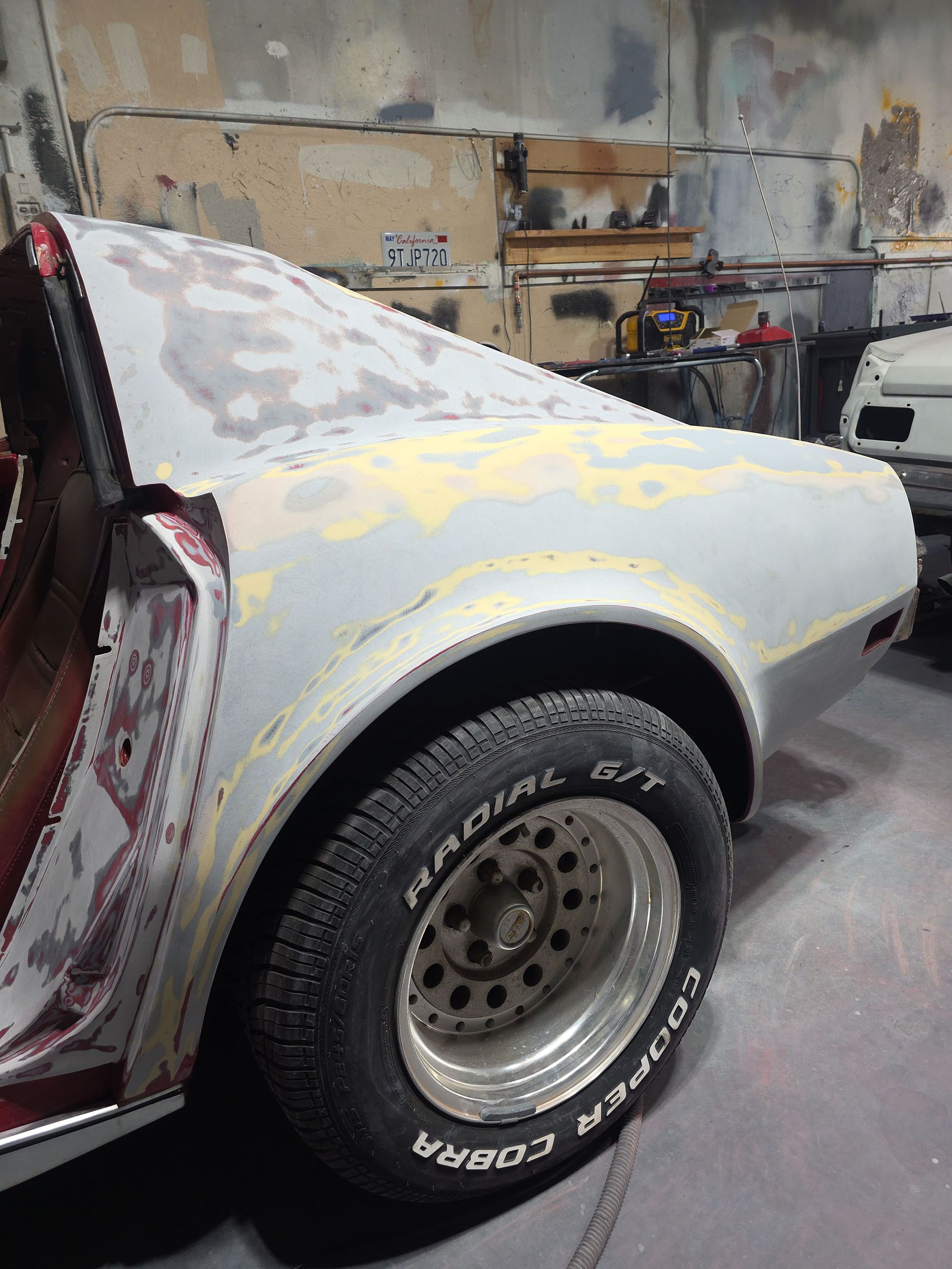 Partially restored gray car body in a workshop, with a rear wheel visible and sanding patches on the panels