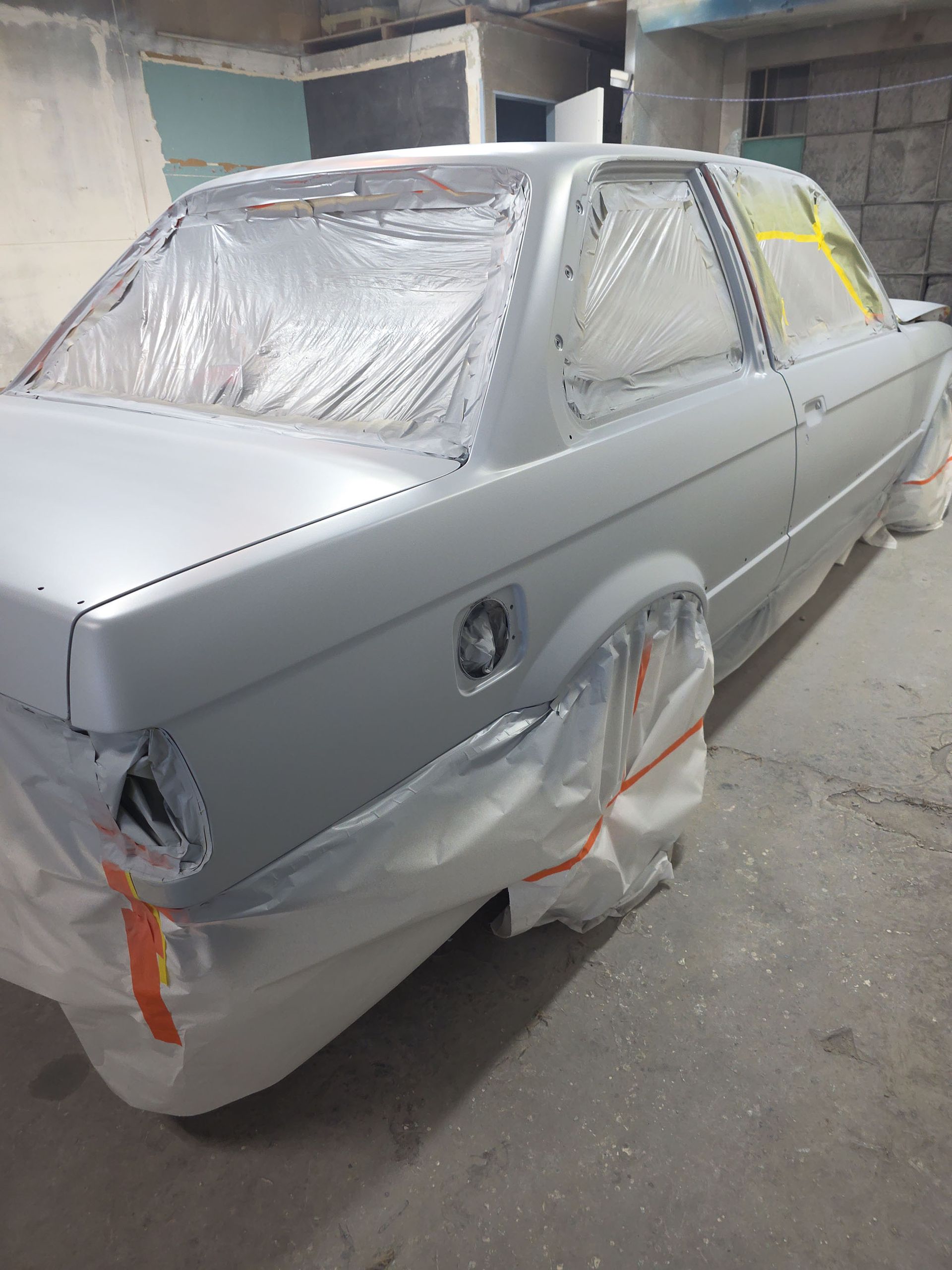 Primer-gray car body in a workshop, masked with plastic and tape for painting repairs.
