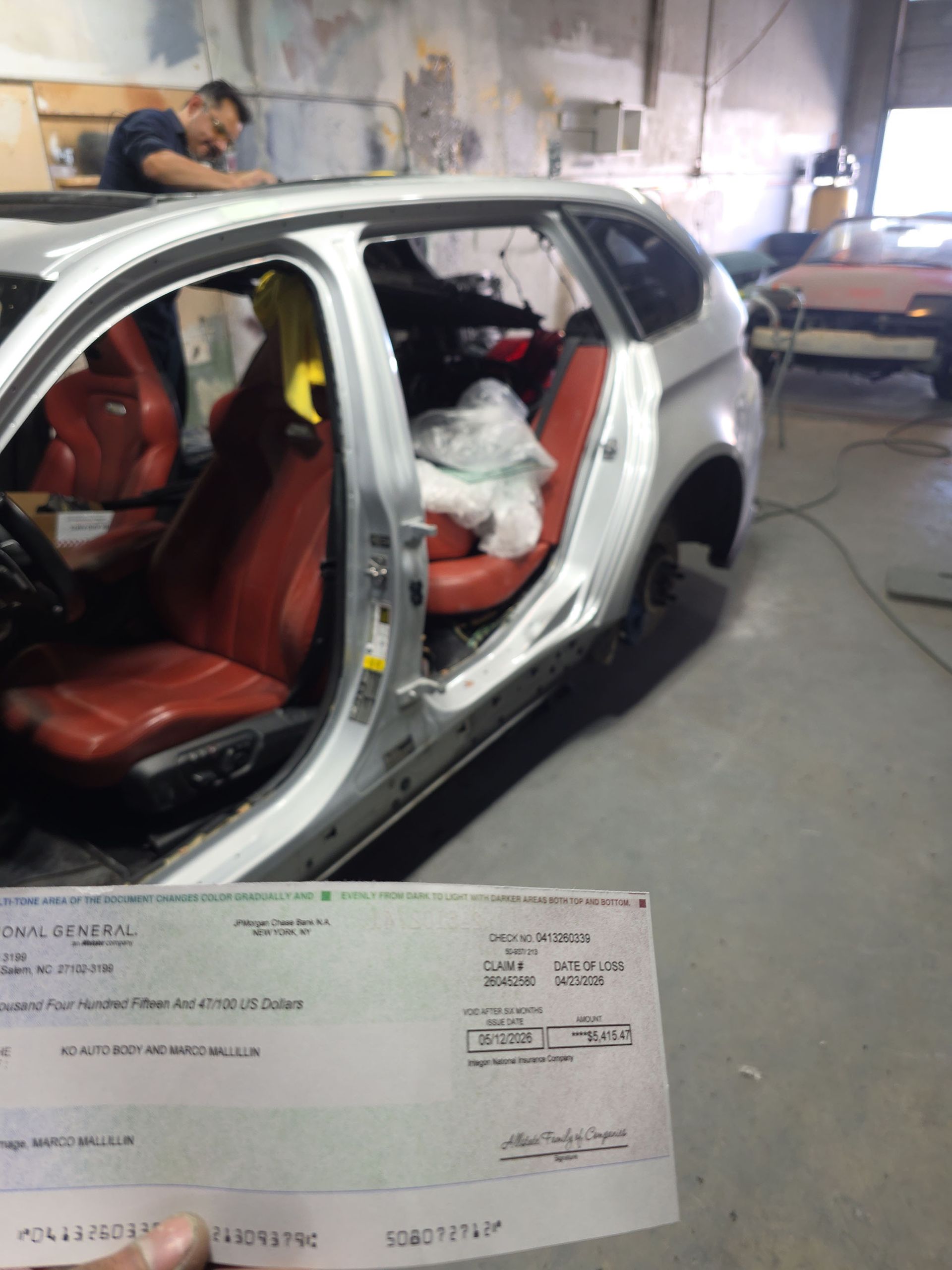 Damaged silver SUV in repair shop with open doors and exposed interior, paperwork in foreground