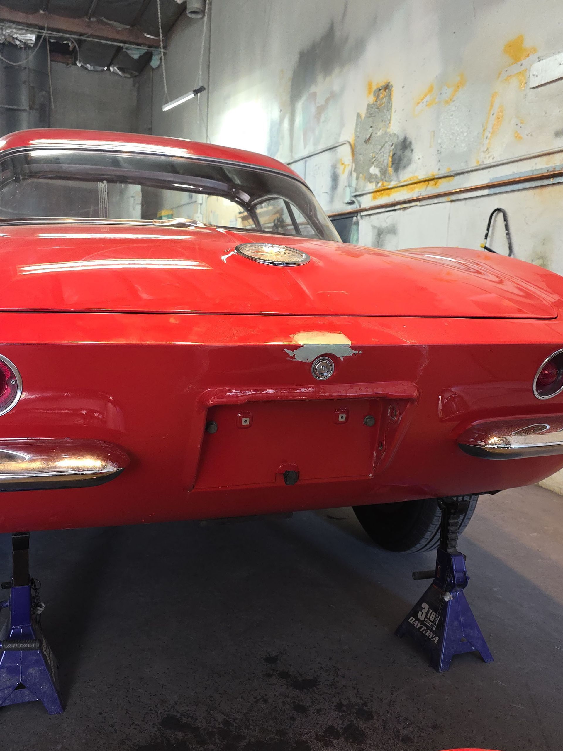 Red classic car rear in a workshop, raised on blue jack stands.