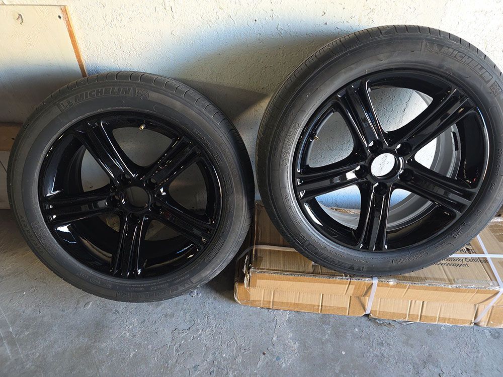 Two black car wheels with tires leaning against a wall on a cardboard box