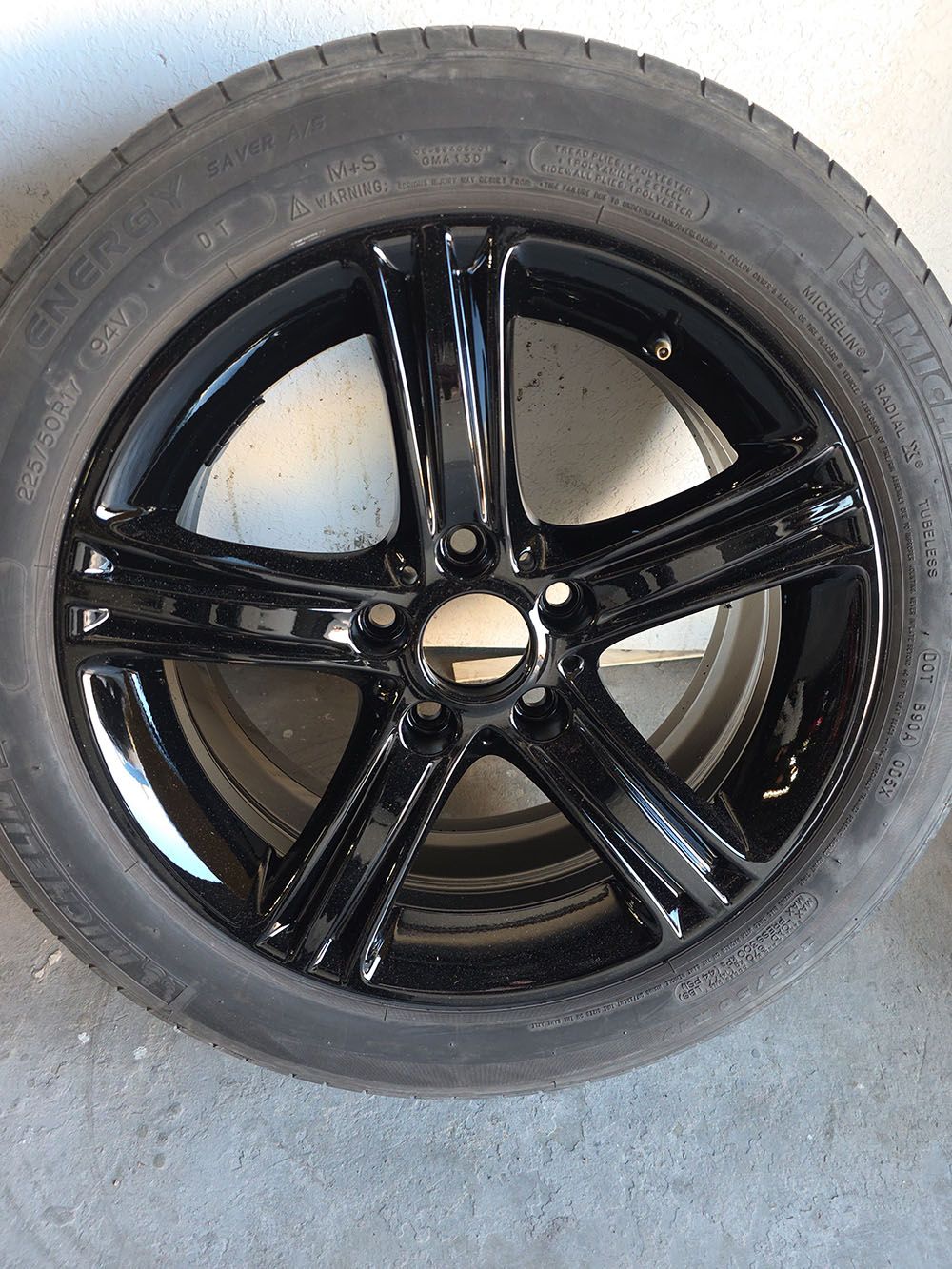 Black five-spoke car wheel with tire, shown against a gray floor.