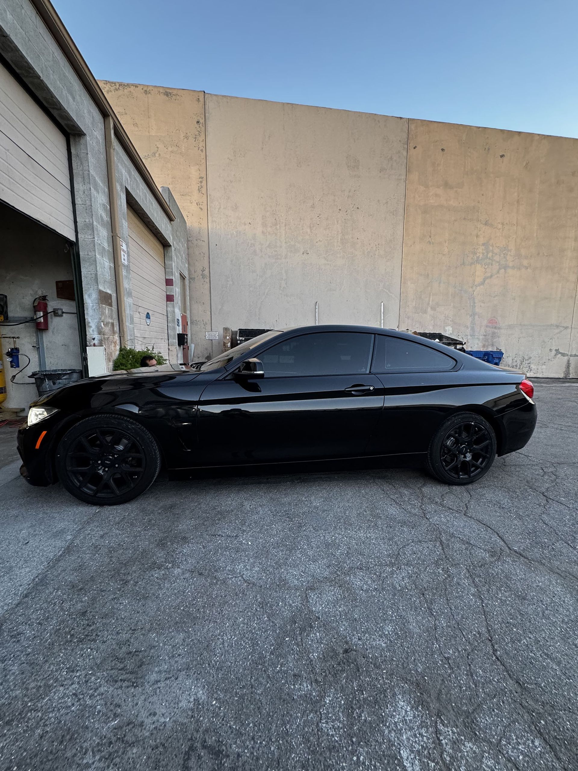 Black sedan parked beside a garage wall in an industrial lot.