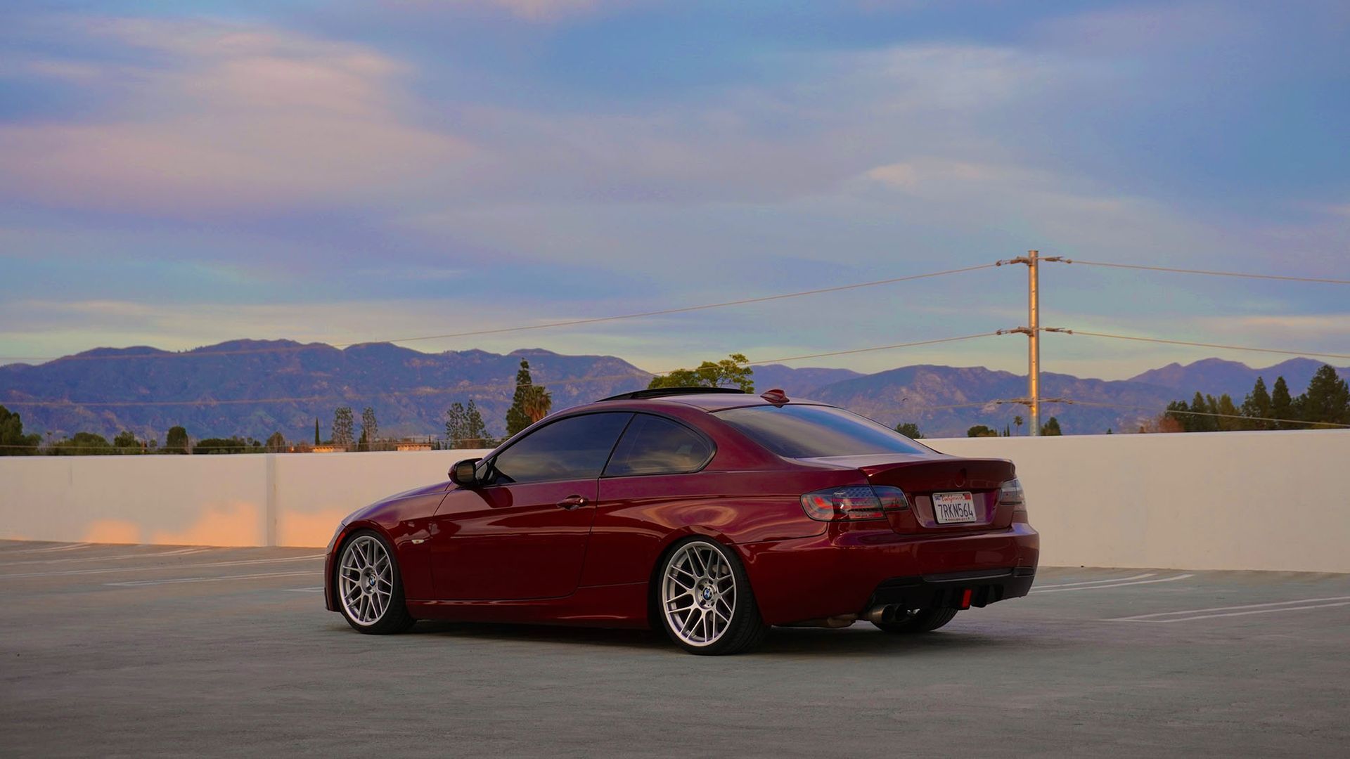 Red sports sedan parked on a rooftop at sunset with mountains in the background