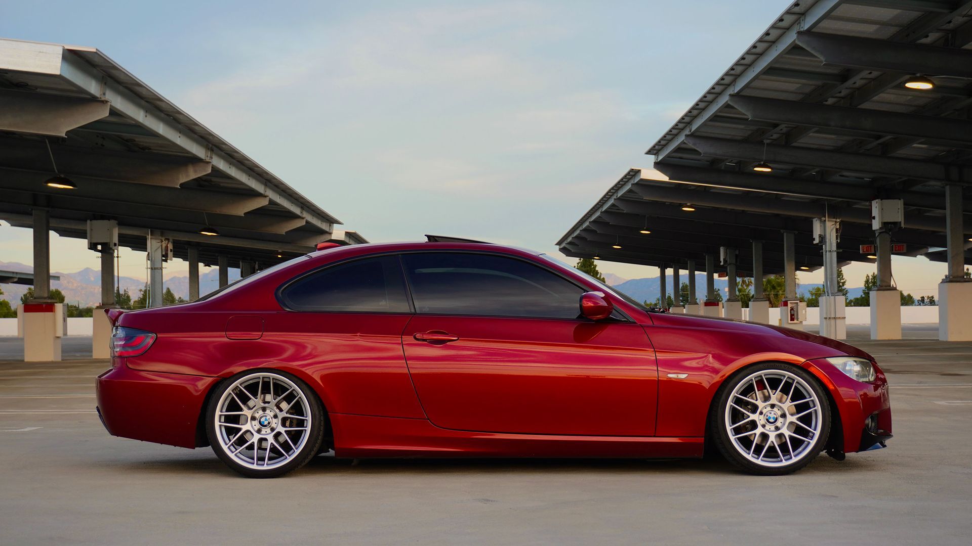 Red sports coupe parked under a covered structure at sunset