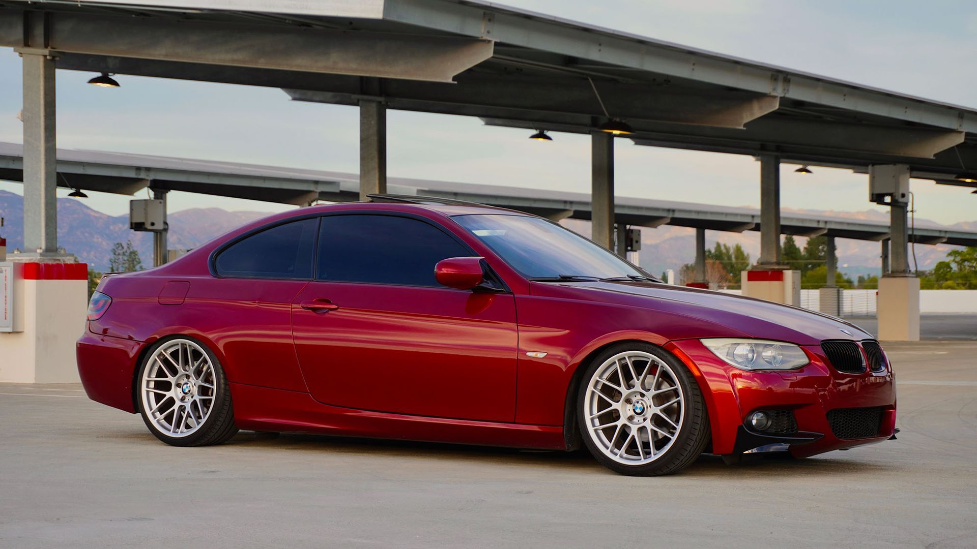 Red modified coupe parked under an overpass at sunset