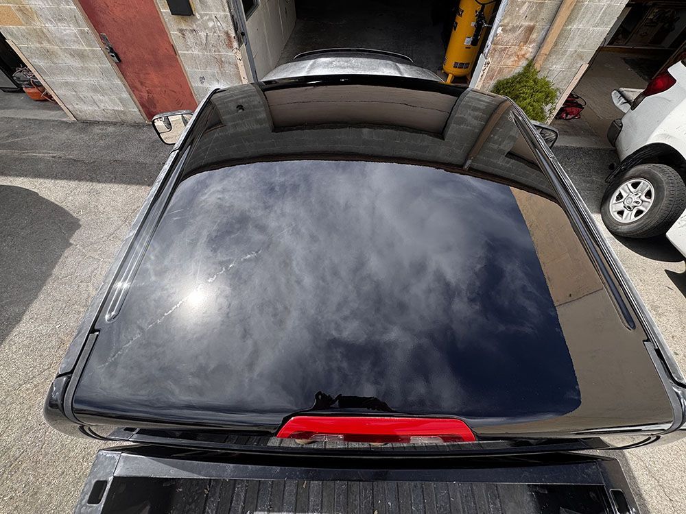 Overhead view of a black car with a reflective roof parked in a narrow garage driveway.