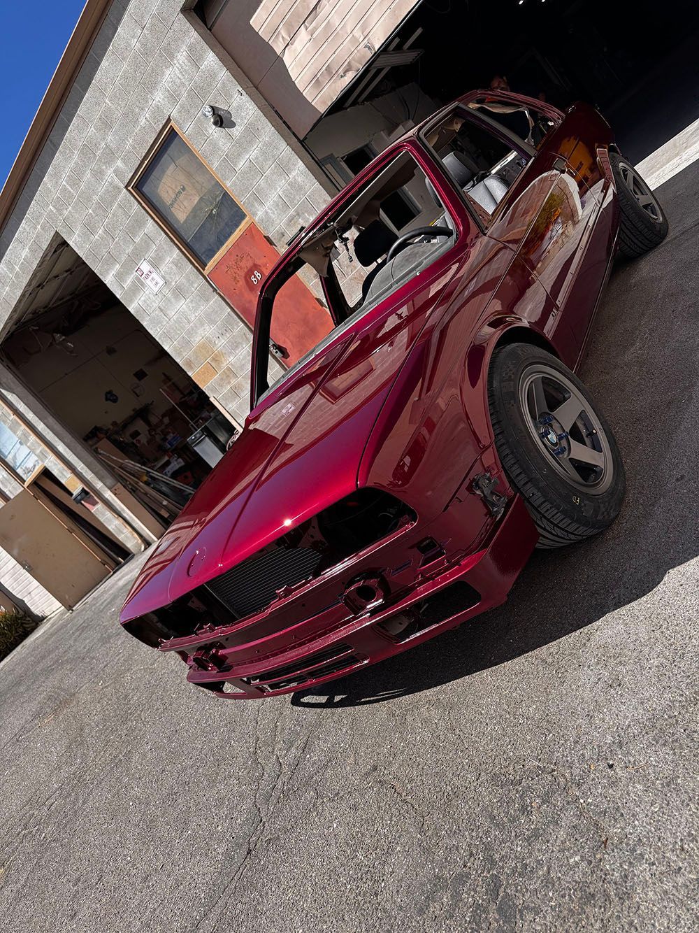 Red vintage convertible coupe parked outside a building, angled on a paved surface.