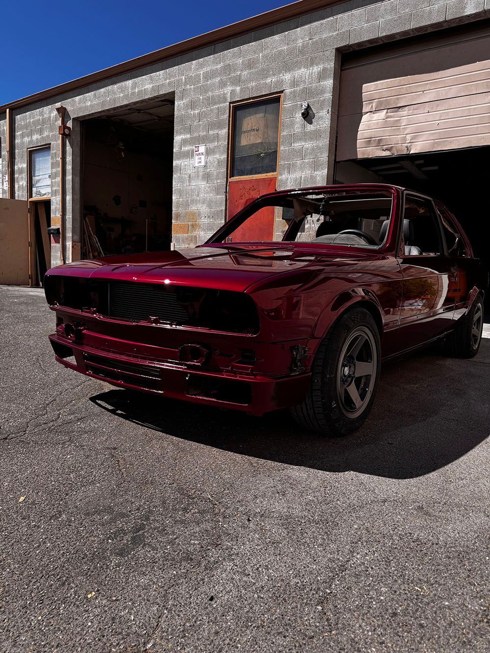 Maroon classic car parked outside a garage with open bay doors