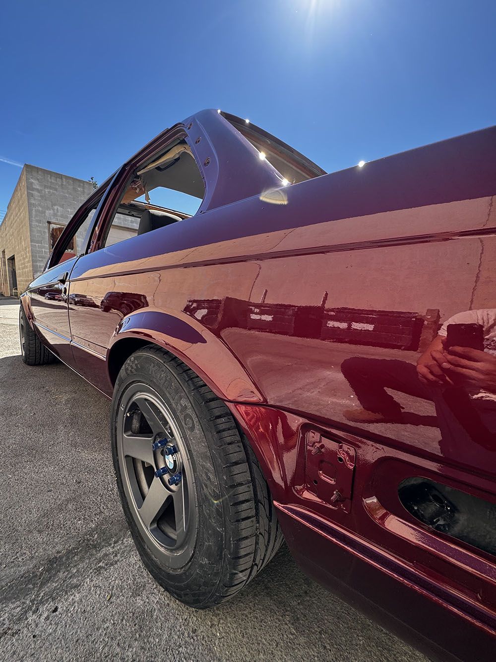 Maroon sports car with black wheels parked outdoors under a bright blue sky.