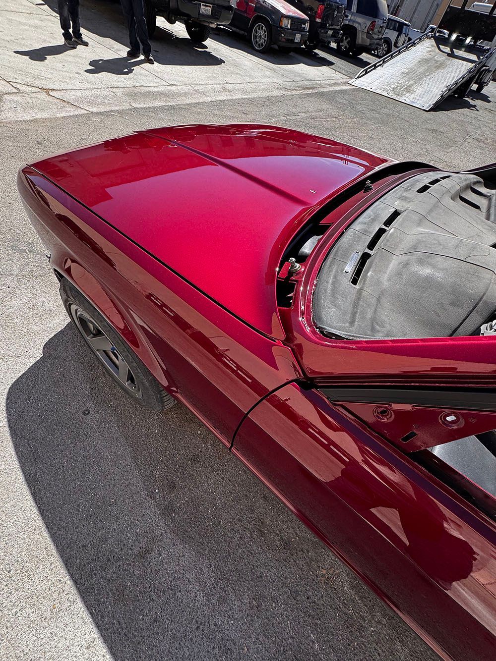 Red convertible with glossy maroon hood parked on gravel, top partially open.