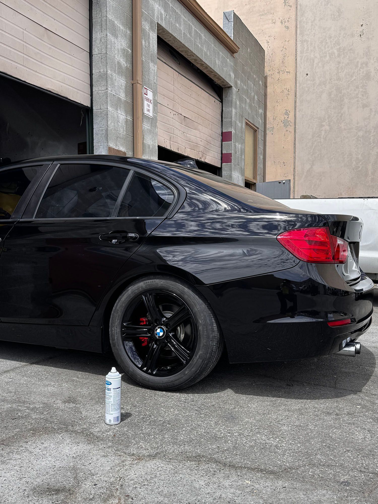 Black sedan parked beside a brick warehouse, with a spray paint can on the pavement nearby.