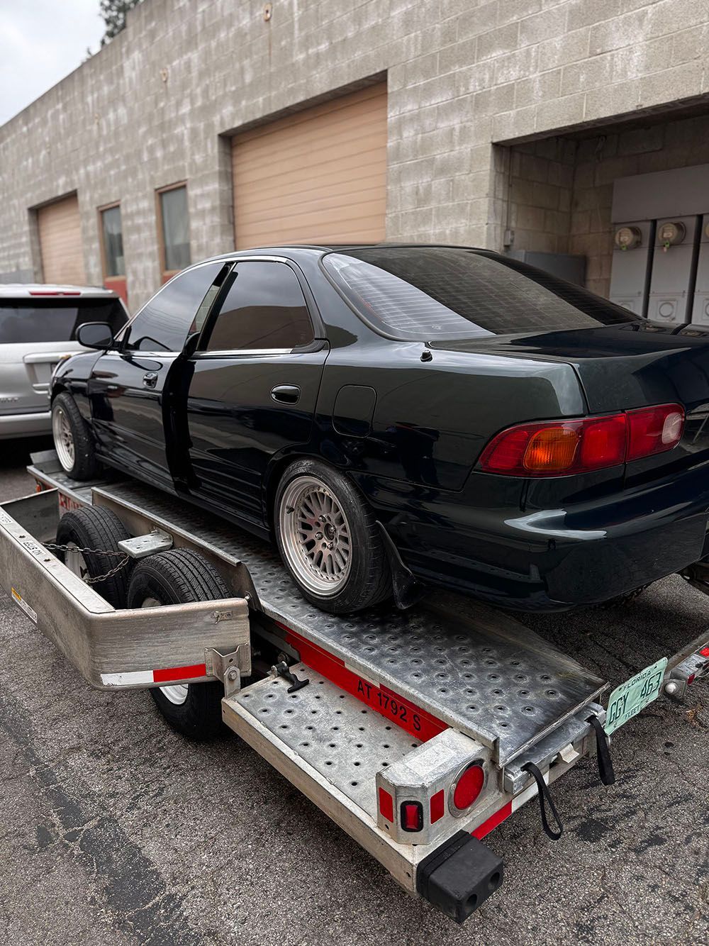 Black sports coupe strapped to a trailer in an industrial lot