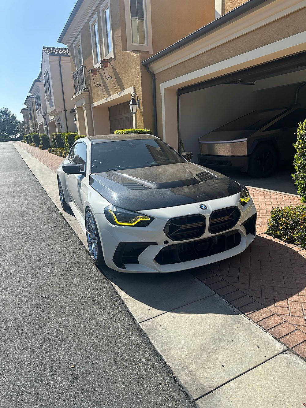 White and black sports sedan parked in a suburban driveway beside a townhouse garage.