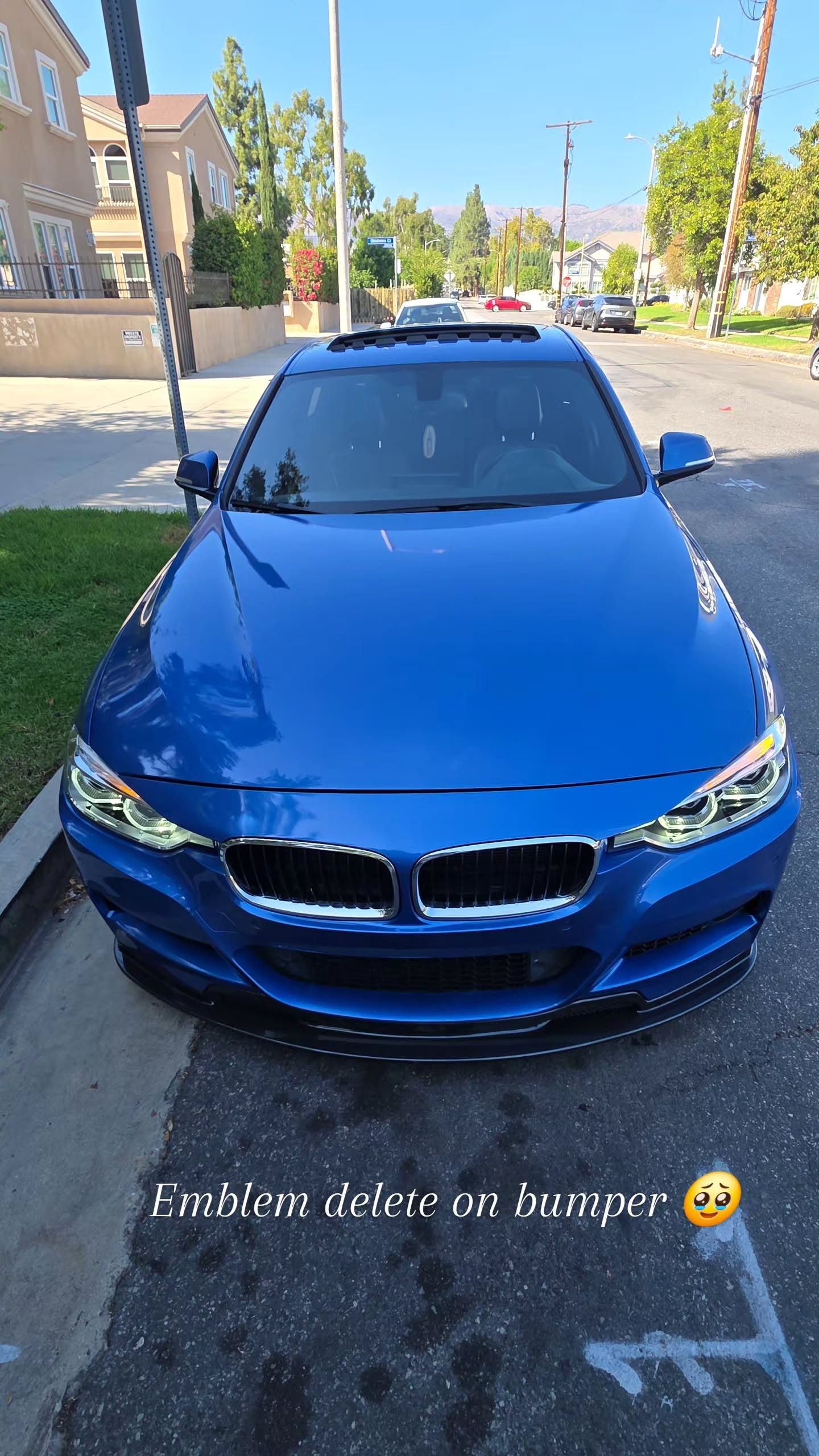 Blue BMW sedan parked on a sunny street with trees and buildings in the background.
