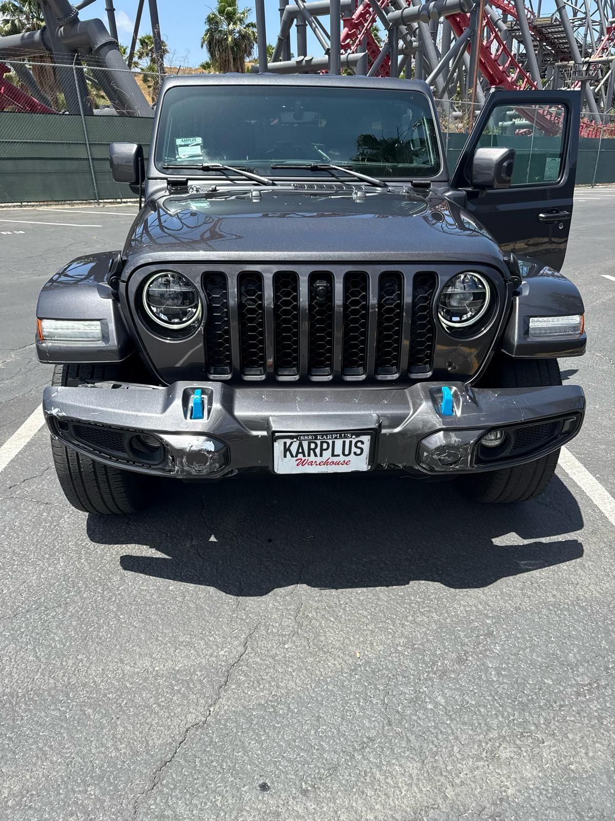 Black Jeep Wrangler facing front in a parking lot, passenger door open, with amusement park rides in the background