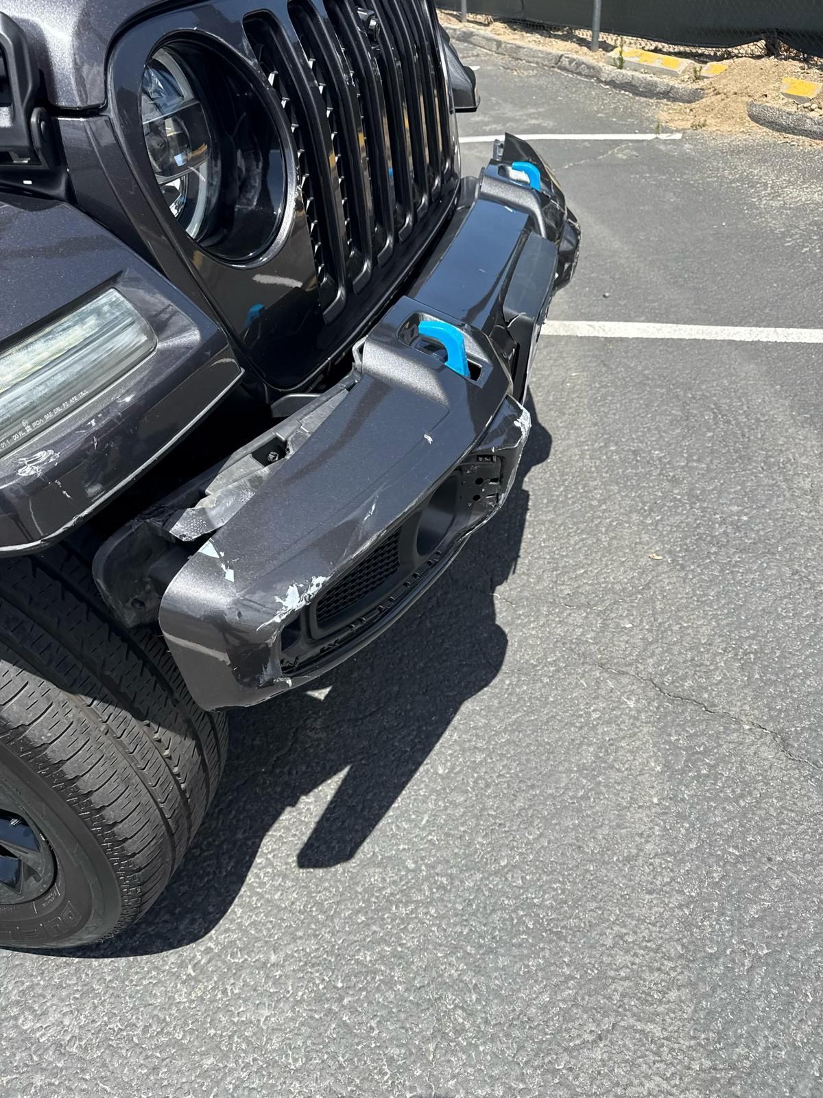 Close-up of a black Jeep bumper with a blue tow strap in a parking lot