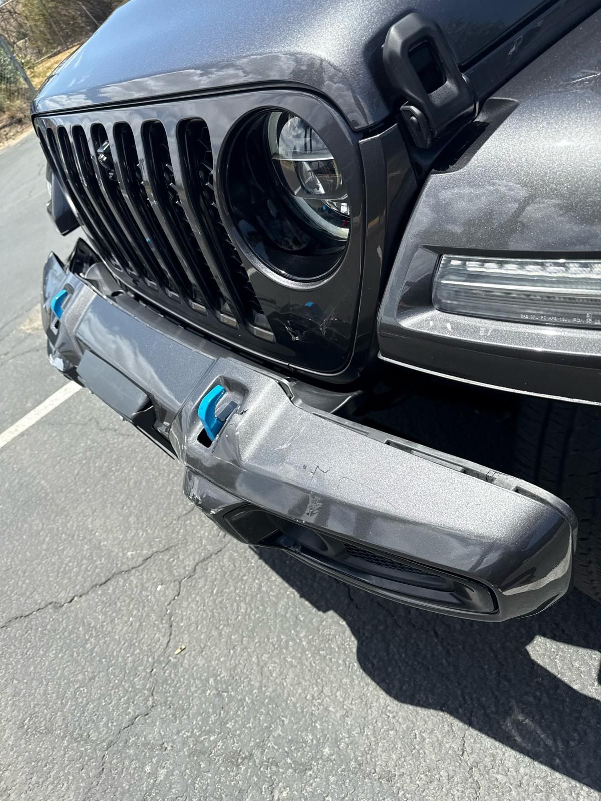 Close-up of a black Jeep’s front bumper and grille with visible damage and a detached bumper piece