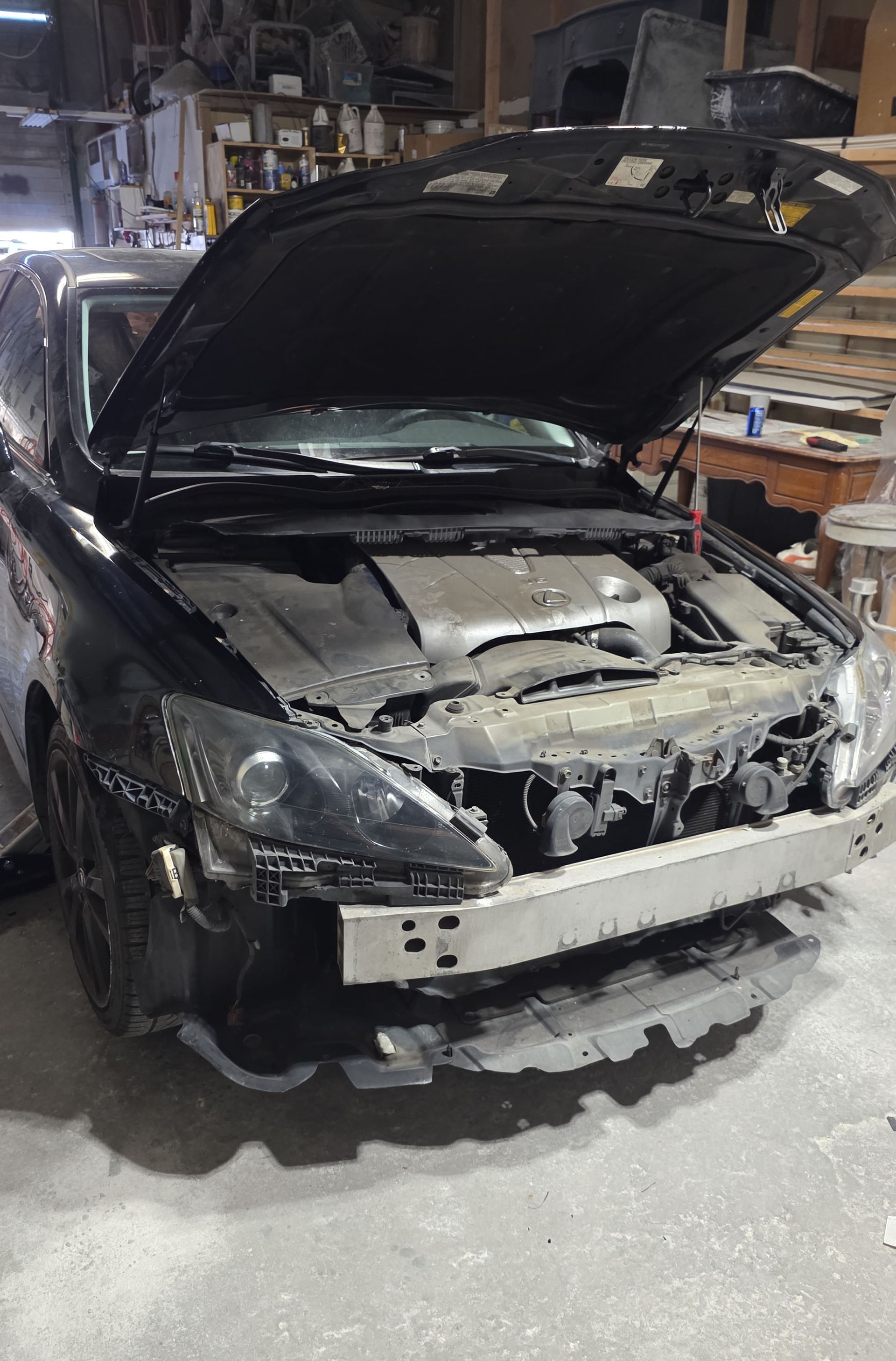 Damaged black car in a garage with hood open and front bumper missing