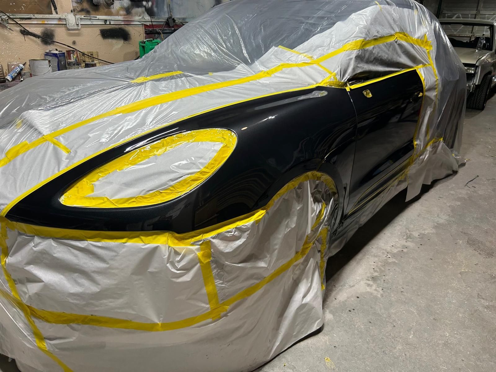 Black car under repair, covered in plastic and masking tape in a workshop