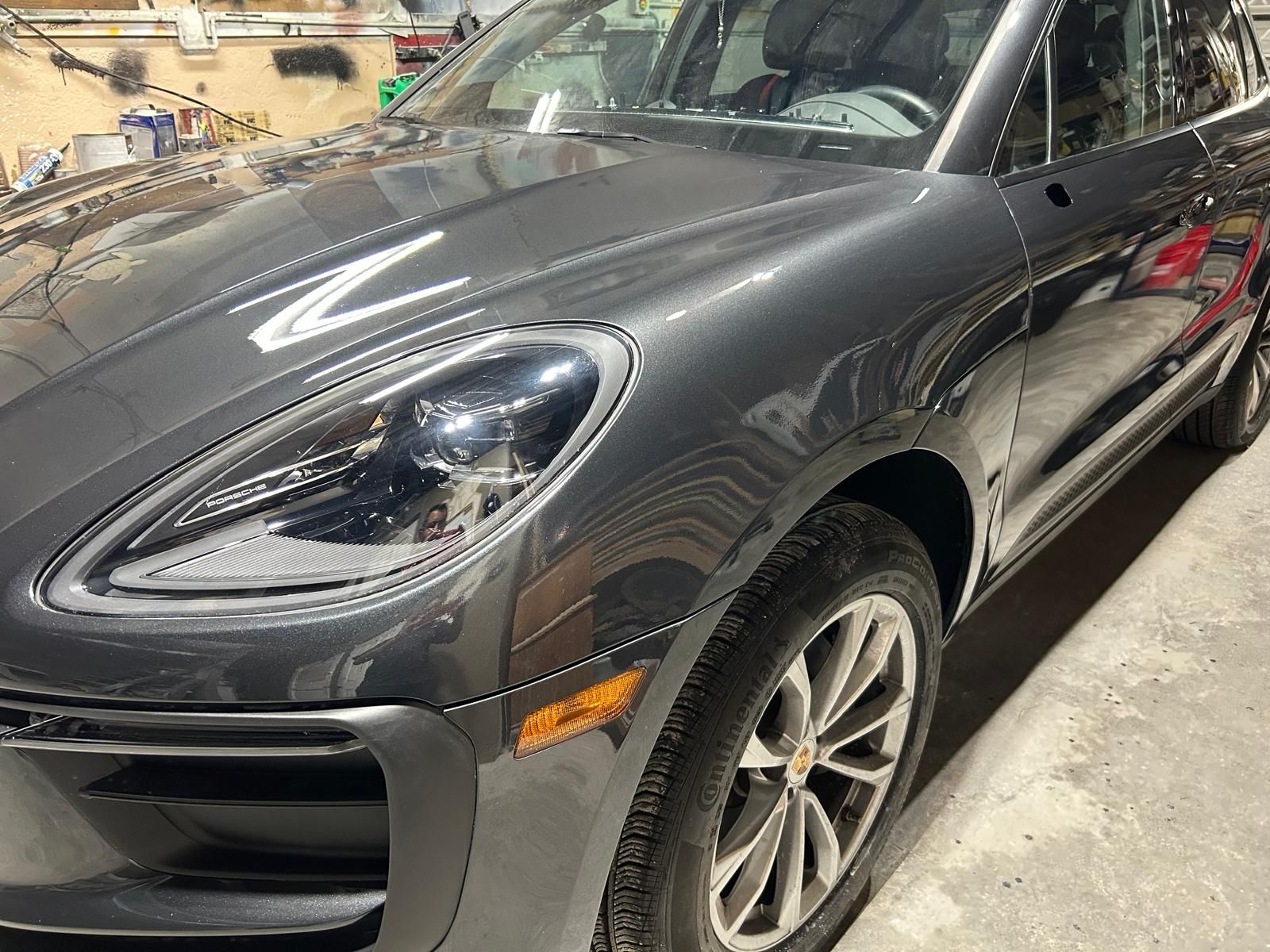 Dark gray Porsche SUV parked indoors, front-left view with visible headlight and wheel.