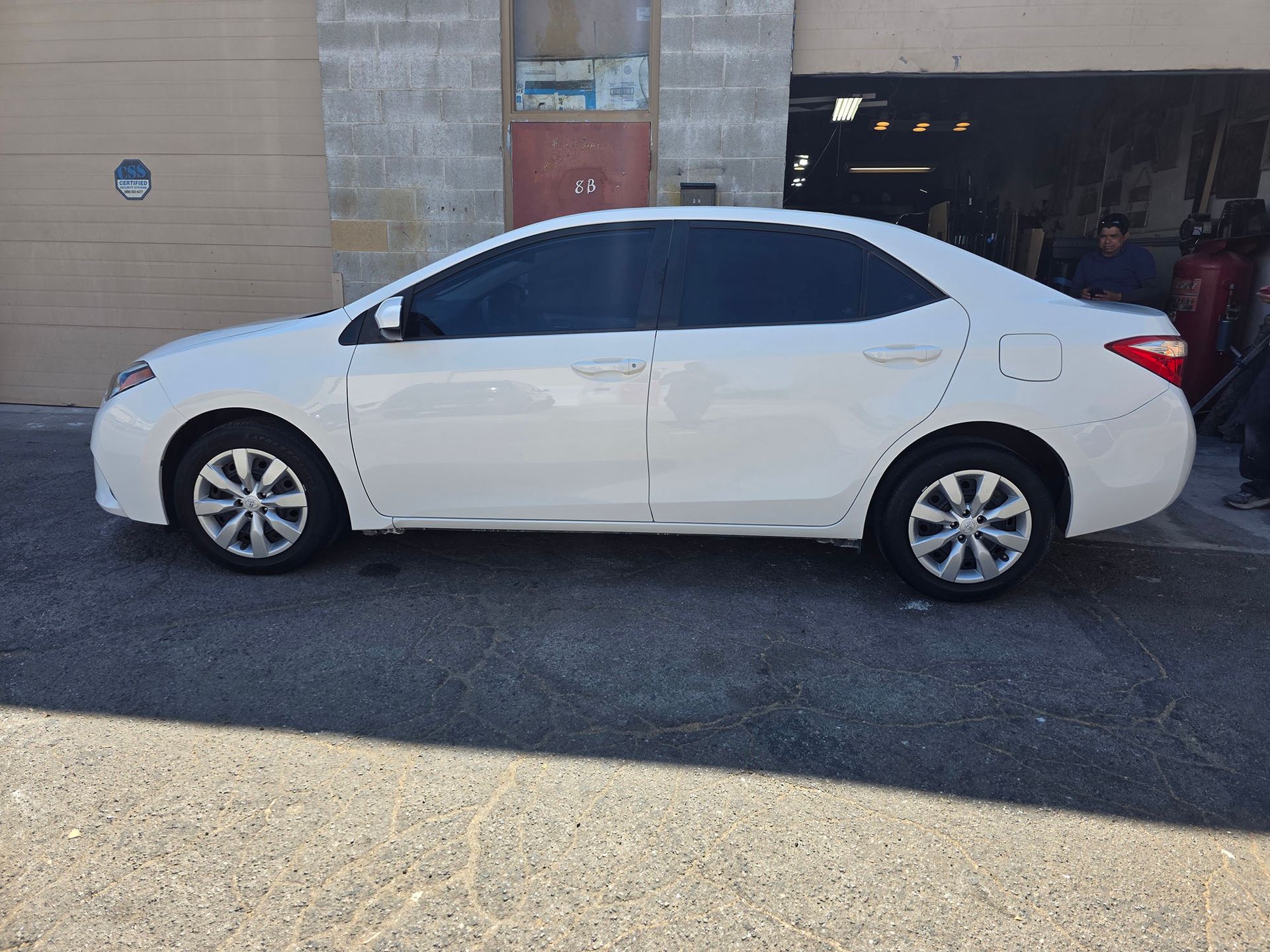 White sedan parked beside a beige building with an open garage door.