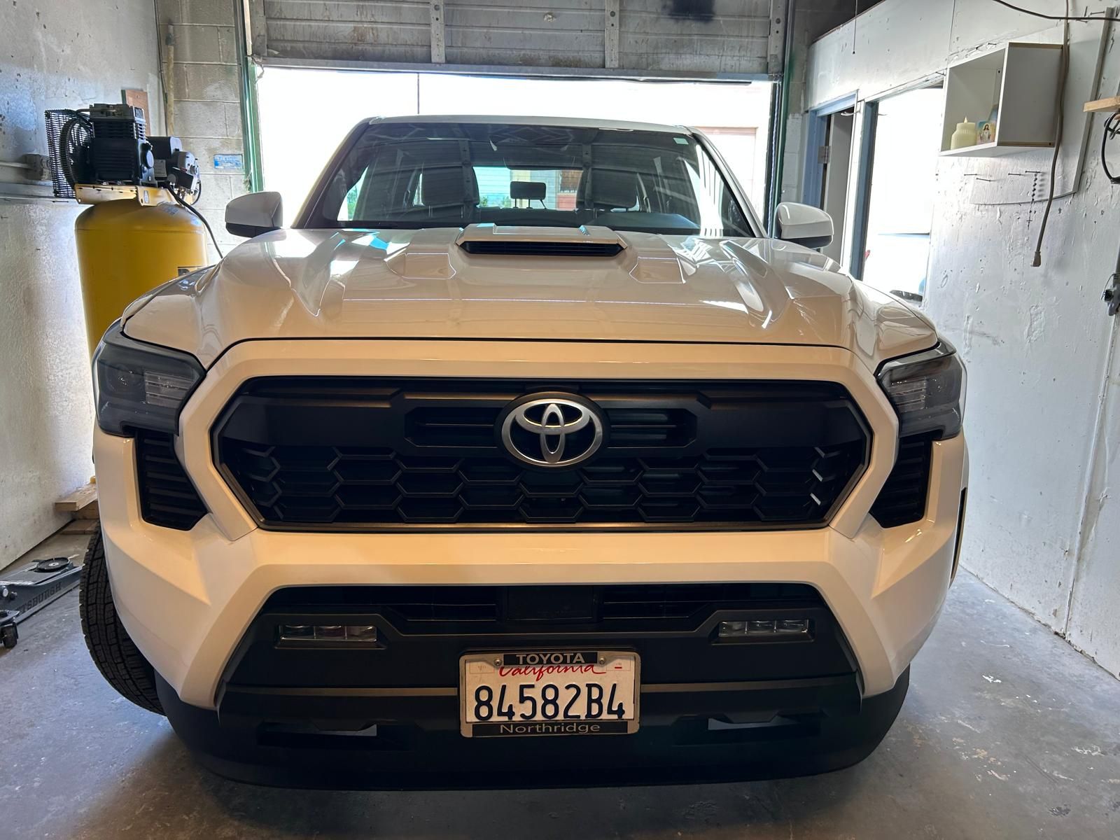 White Toyota Tacoma parked in a garage, front view with a visible license plate.