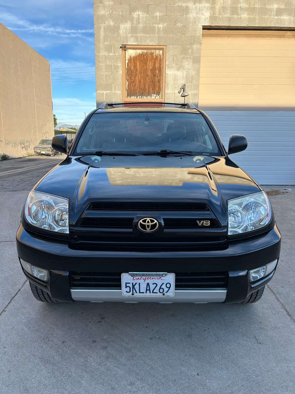 Black Toyota SUV parked in an industrial lot, front view with a garage door and wall behind it.
