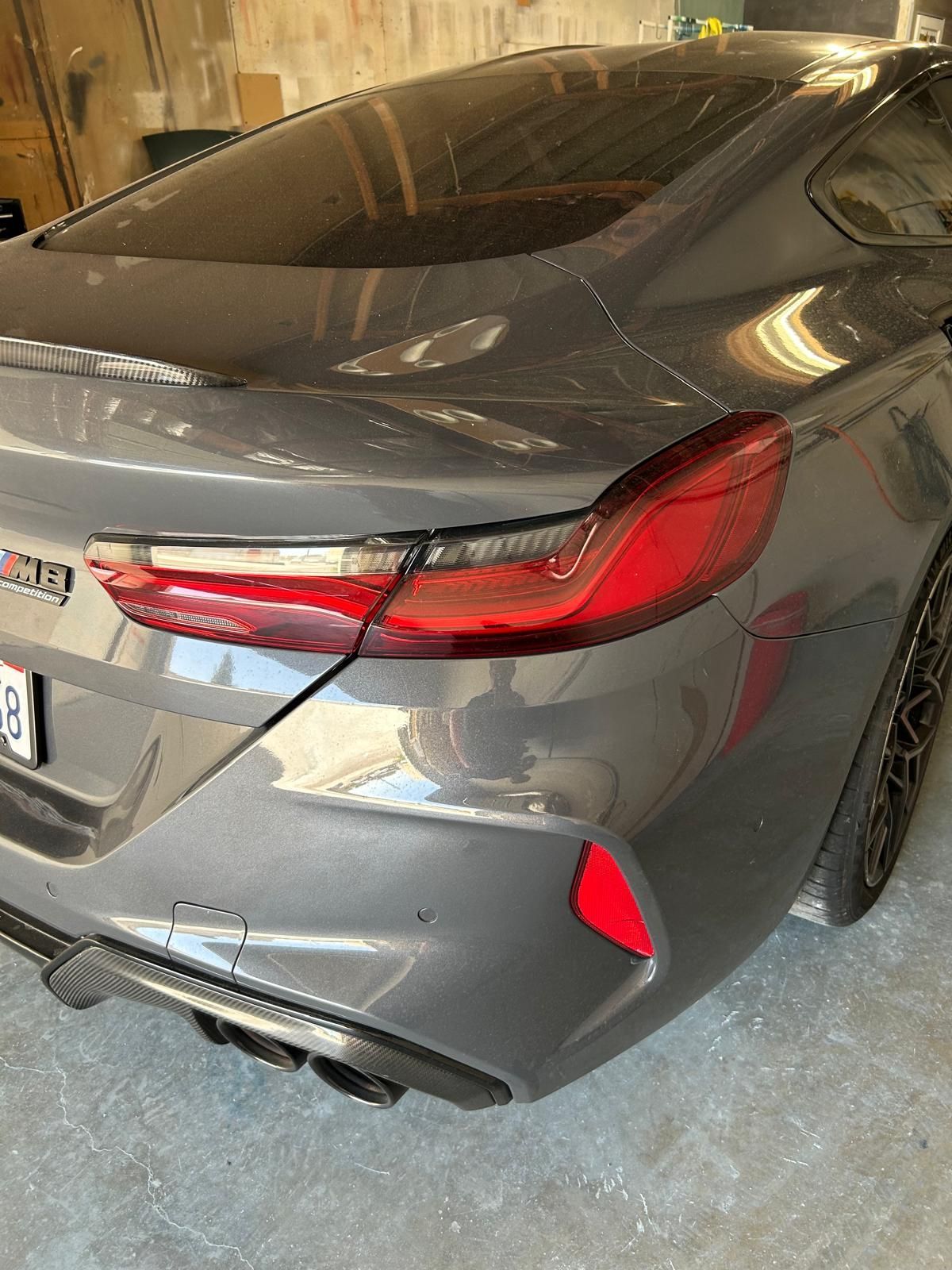 Rear view of a gray sports car in a garage, showing a red taillight and rear bumper