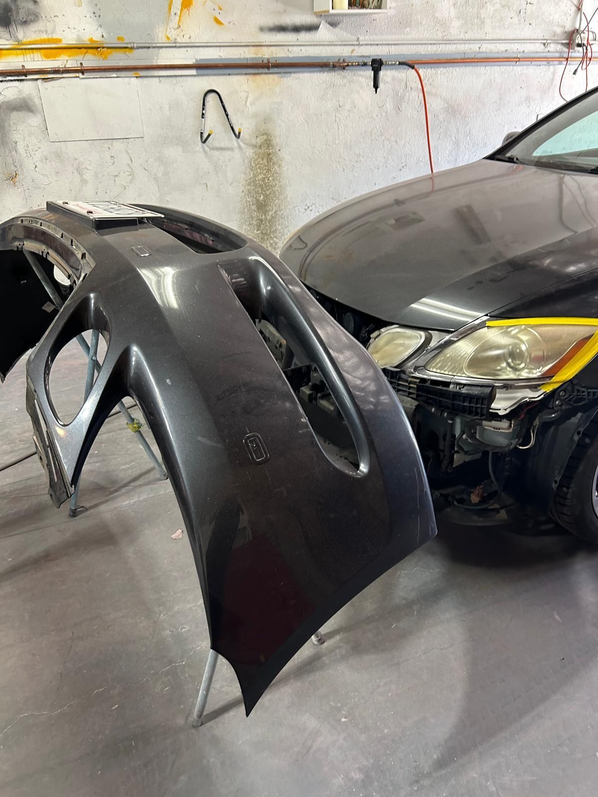 Detached car bumper beside a black car in a garage.
