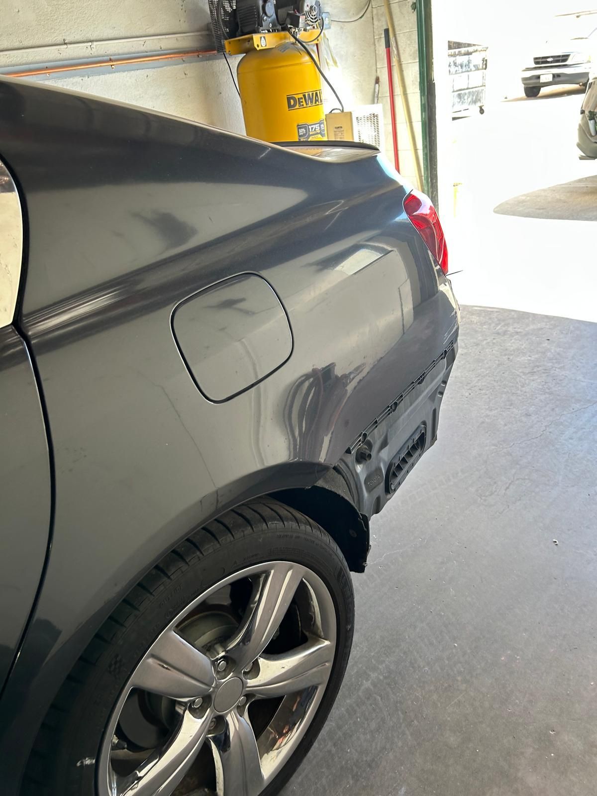 Close-up of a gray car’s rear side and wheel in a garage, with fuel door visible.
