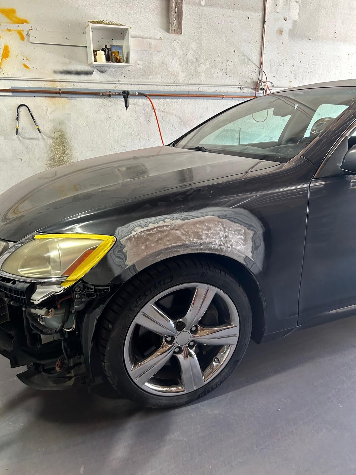 Black car with damaged front-left fender and headlight in a garage.