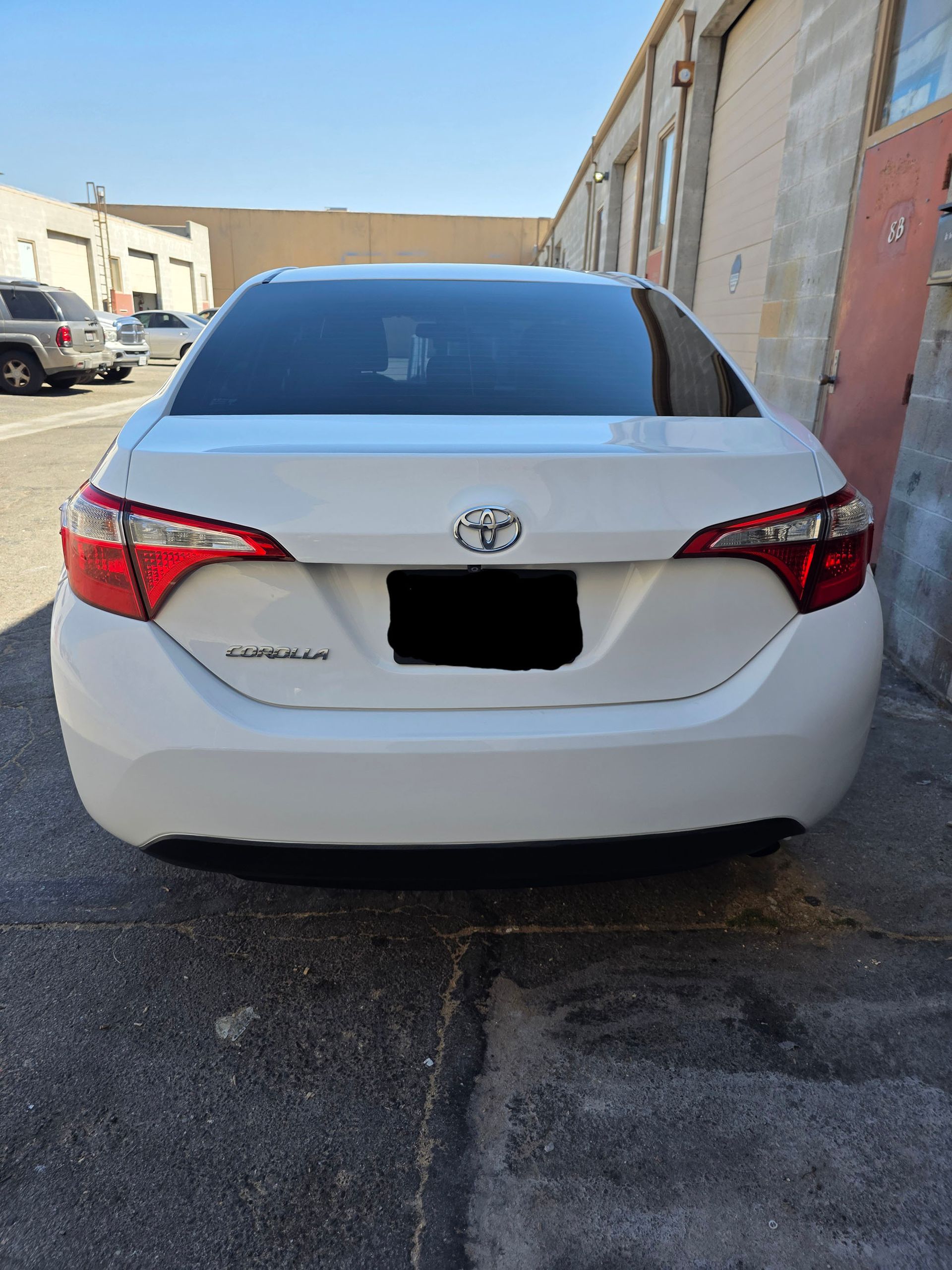 Rear view of a white Toyota sedan parked in an alley beside buildings.
