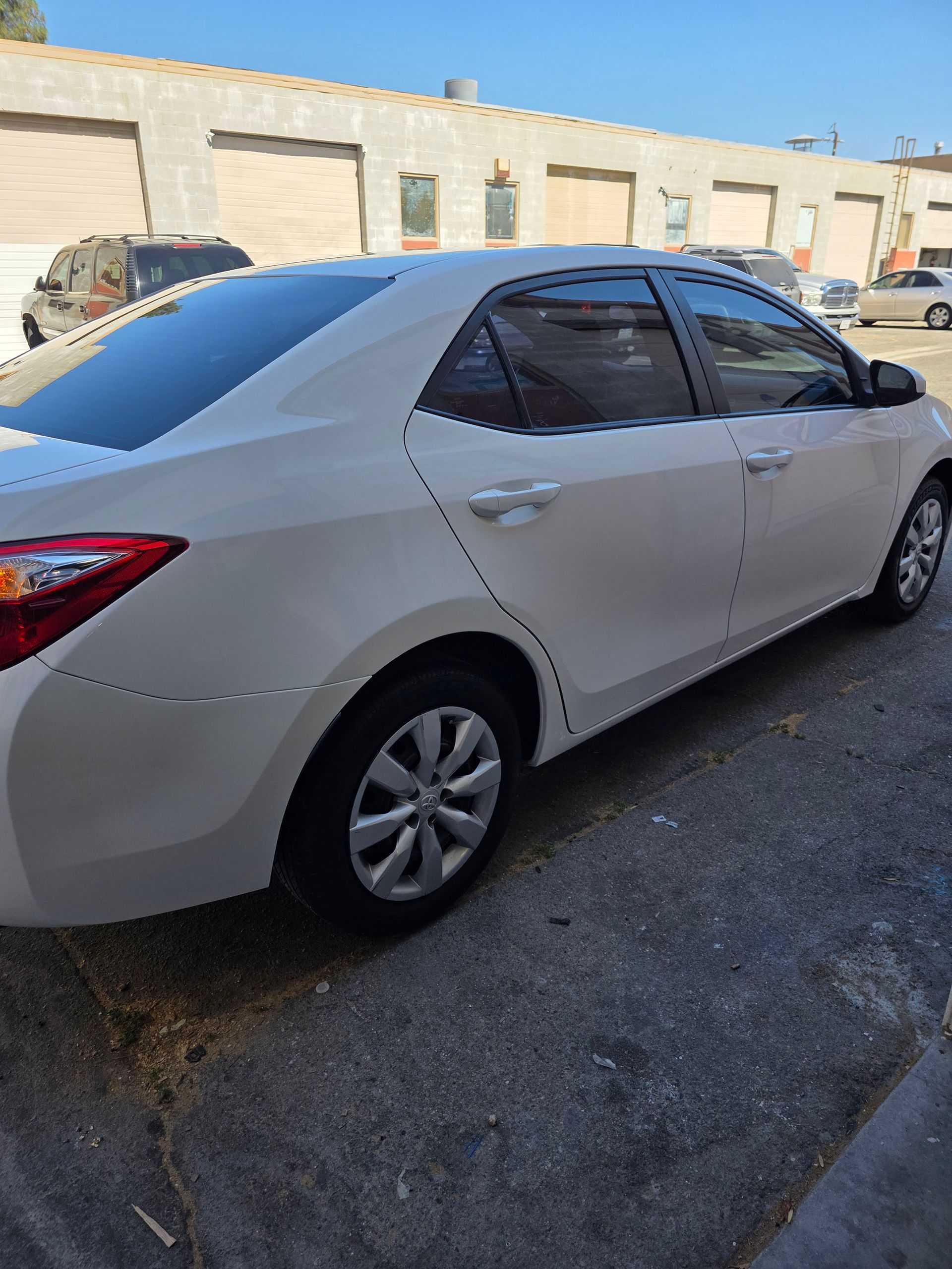 White sedan parked on a street beside beige buildings in bright daylight