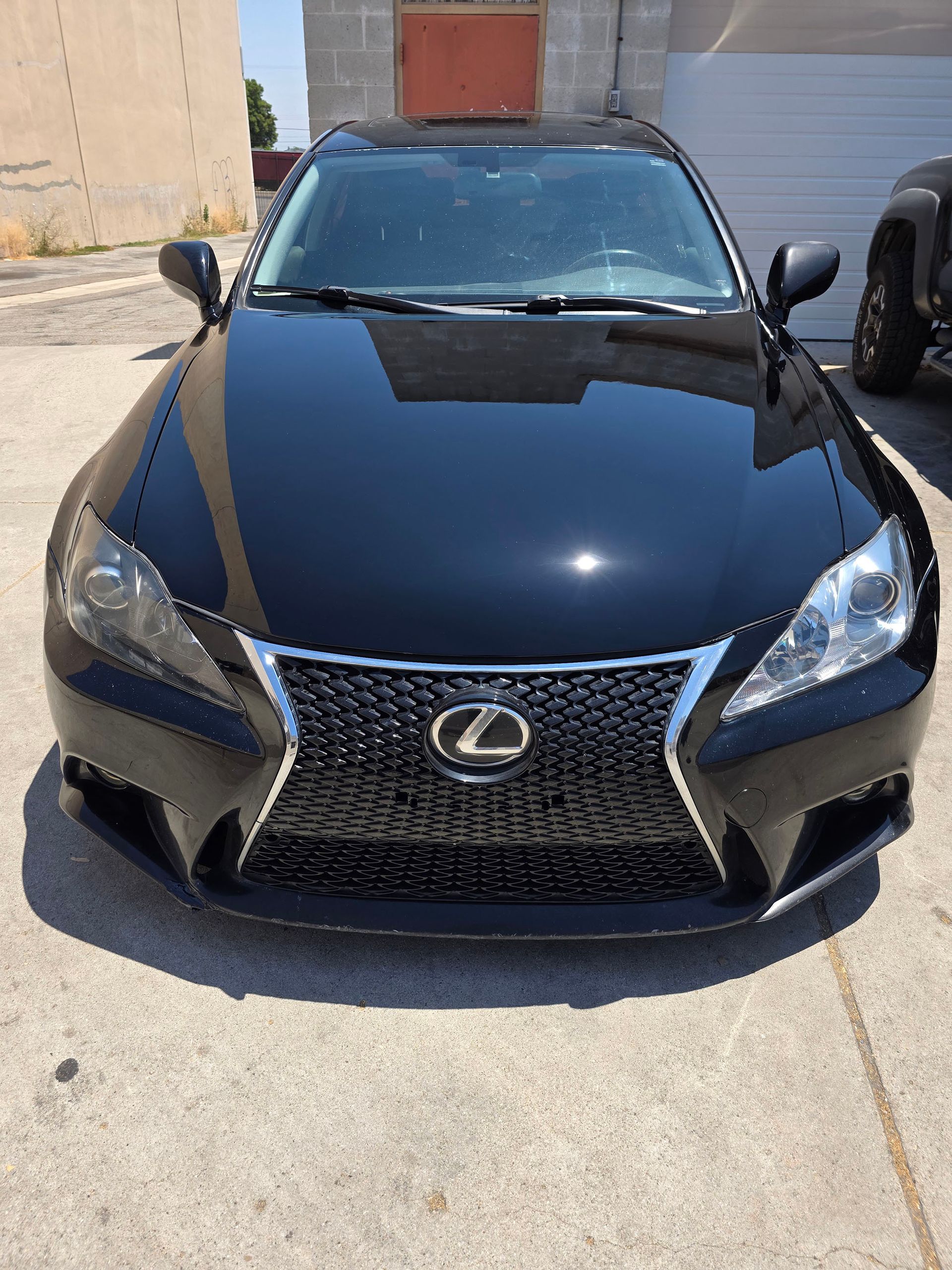 Black Lexus sedan parked in a driveway, front view under bright sunlight.