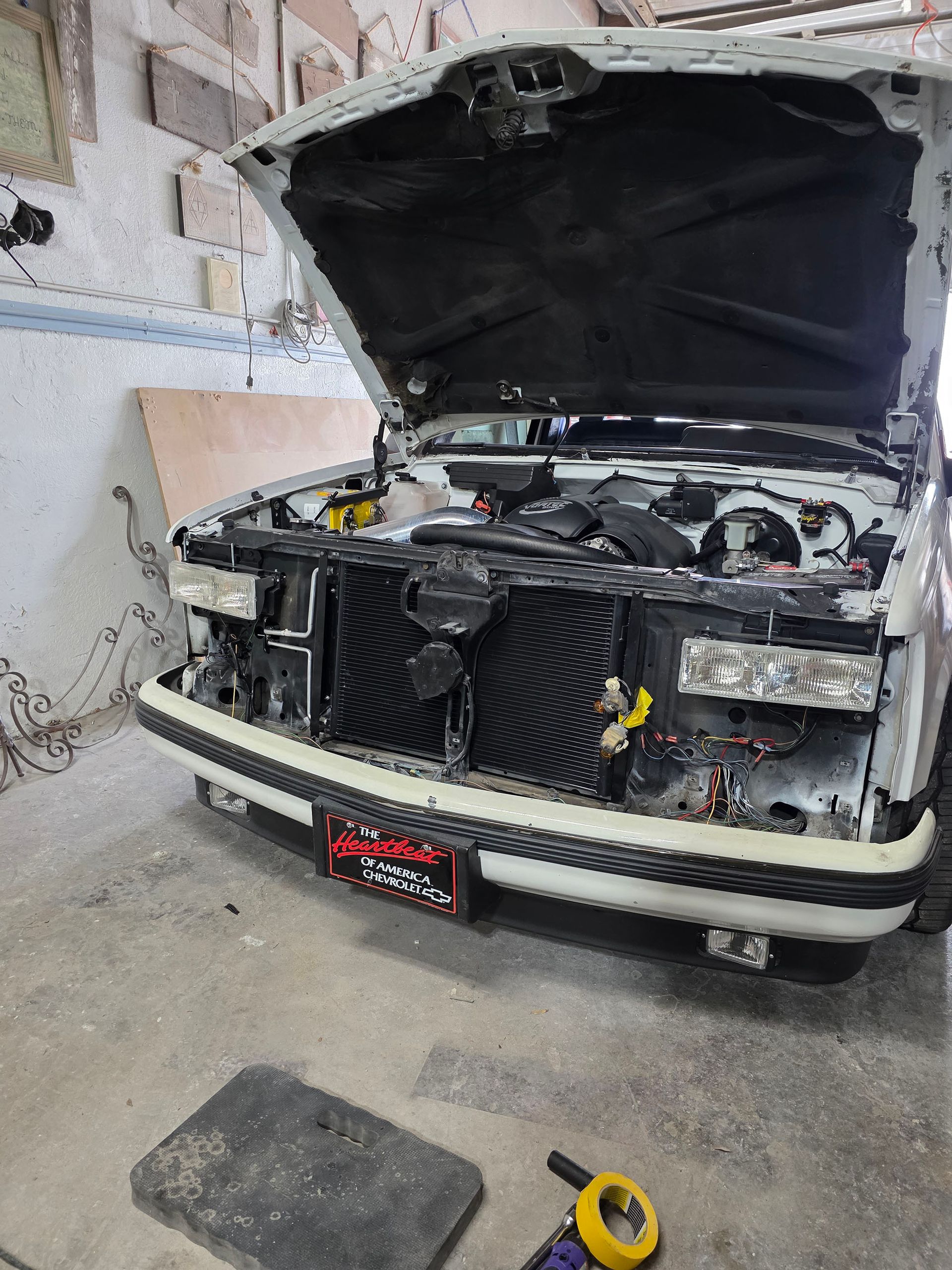 Black car with hood open in a garage, front grille removed and engine exposed.