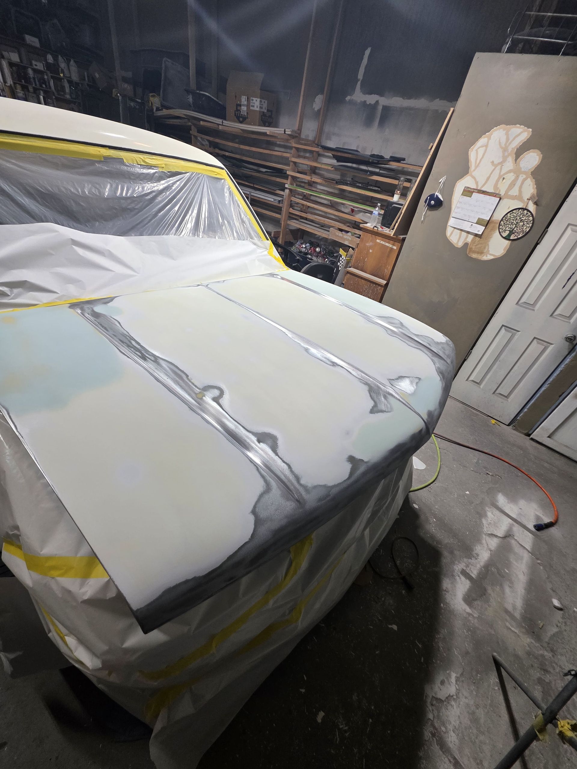 Car covered in masking plastic and tape inside a garage during repair or painting