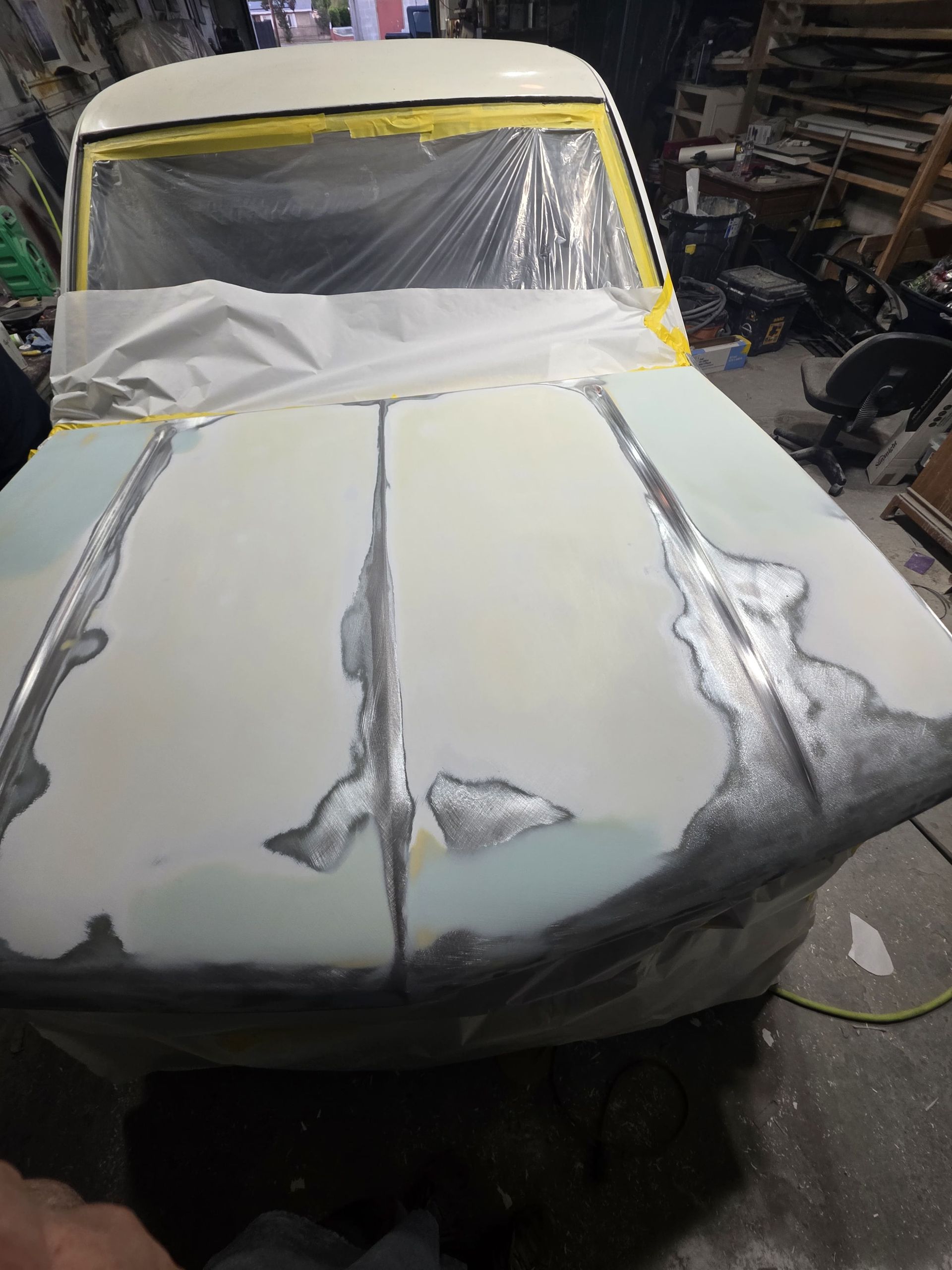 Partially restored white car body in a workshop, covered with primer and taped windows