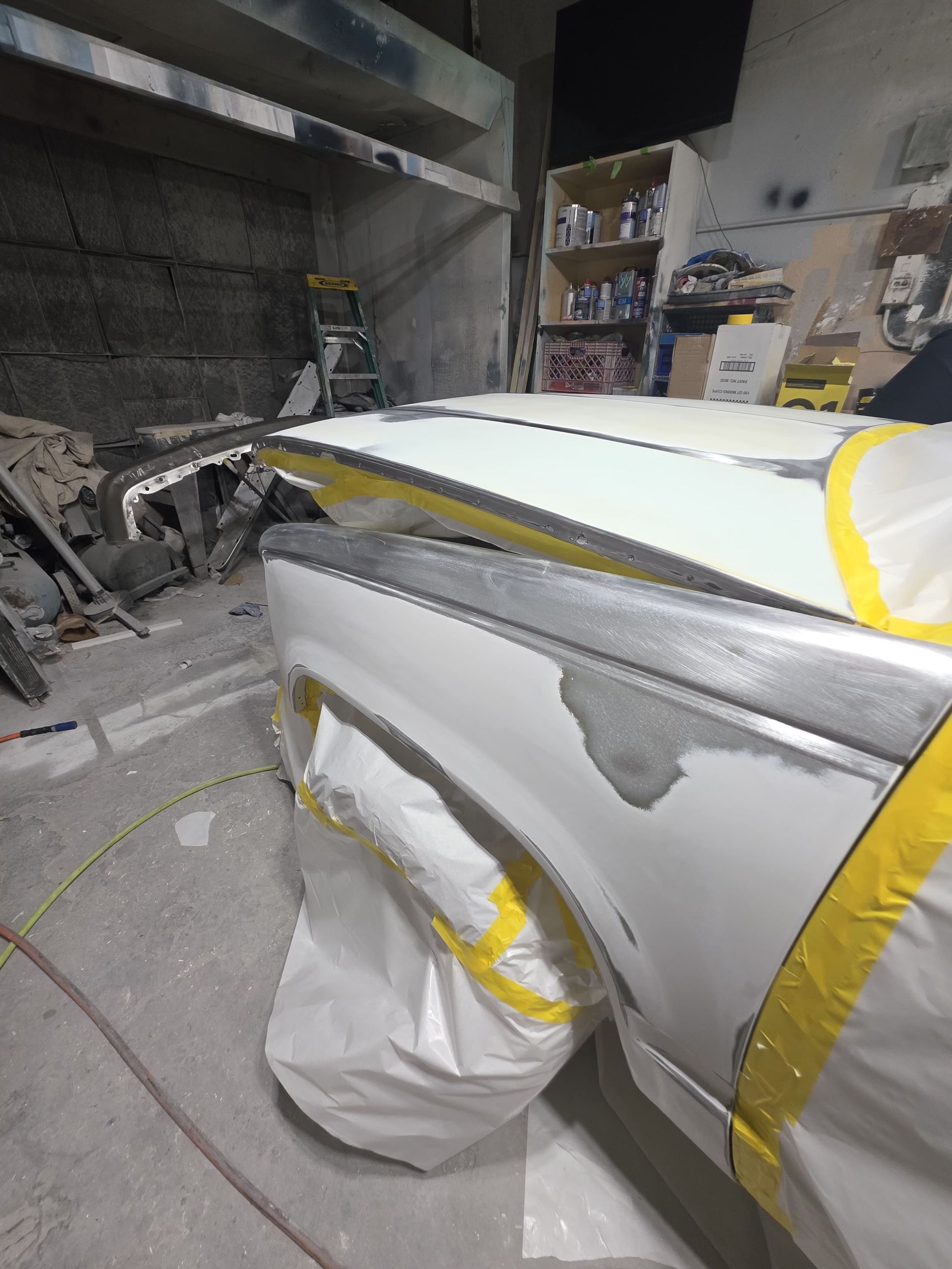 Auto body shop with a car wrapped in plastic and yellow tape inside a spray booth