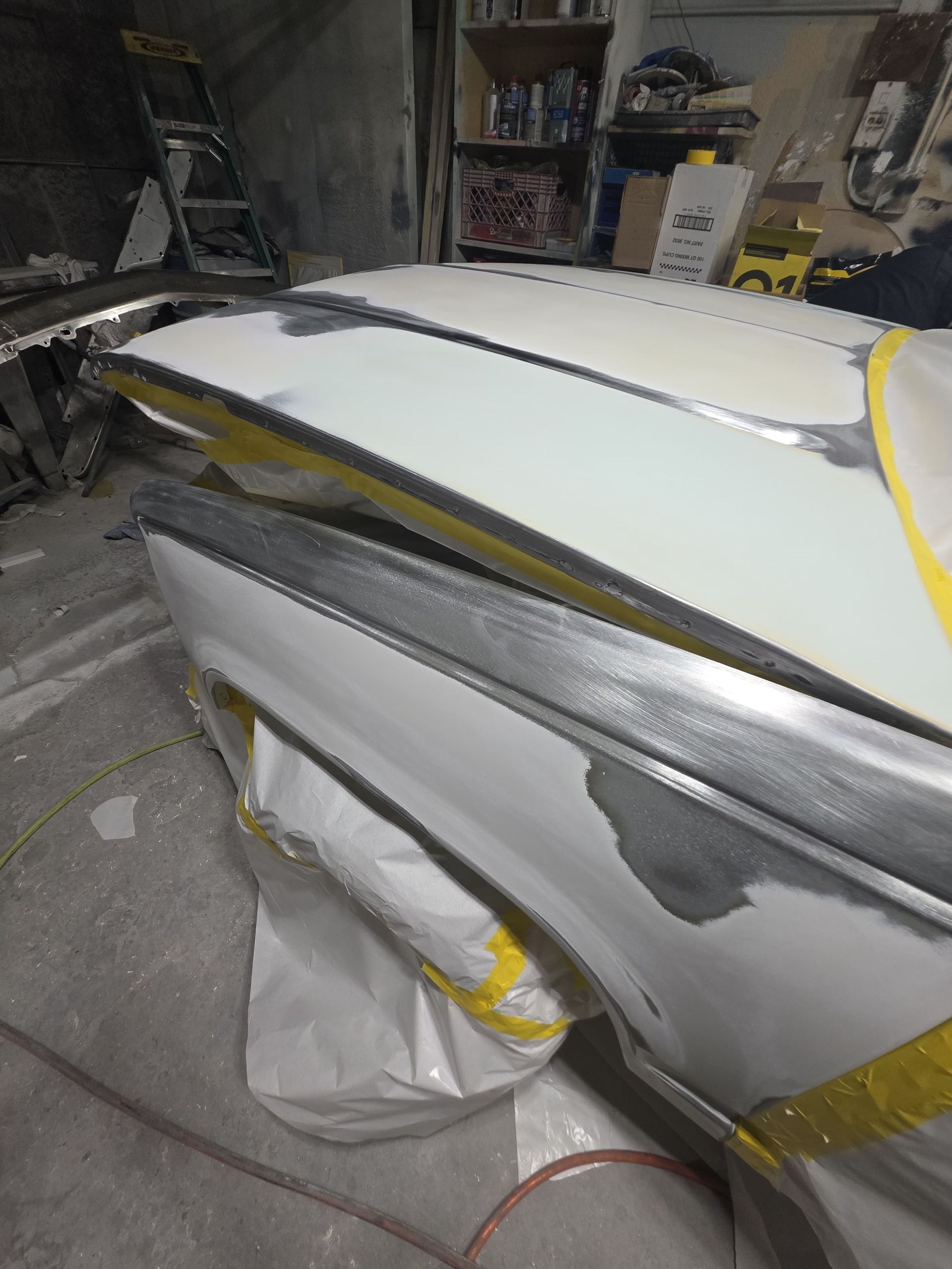 Partially masked white car panel in a workshop with yellow tape and sanding dust